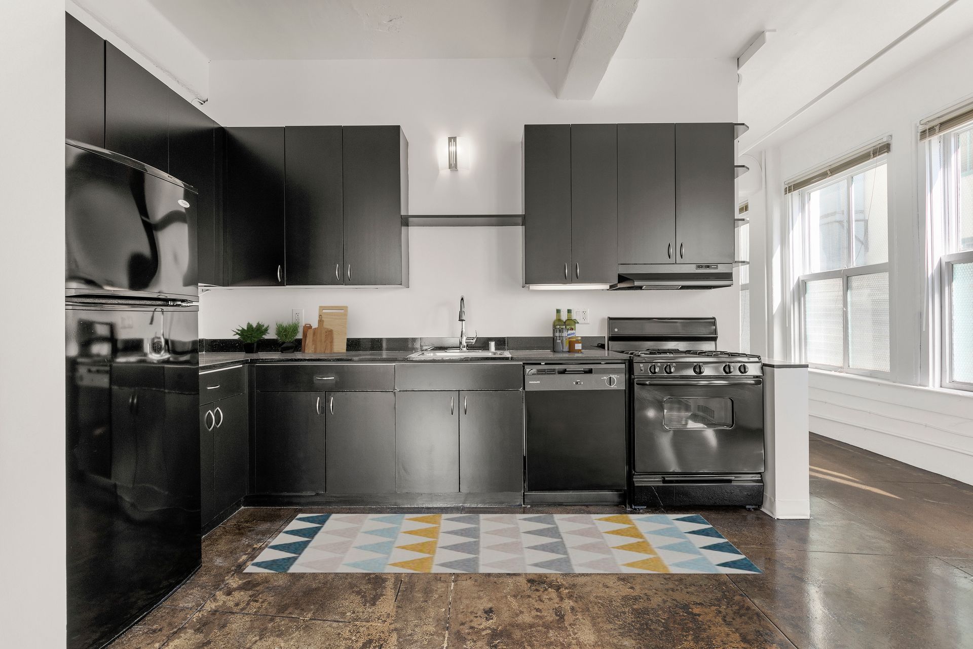 Modern kitchen with black cabinets, stainless appliances, and a colorful rug by bright windows