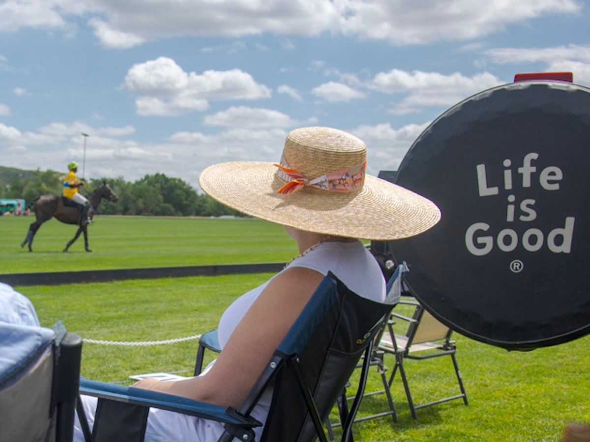 A woman in a straw hat sits in a chair watching a polo match