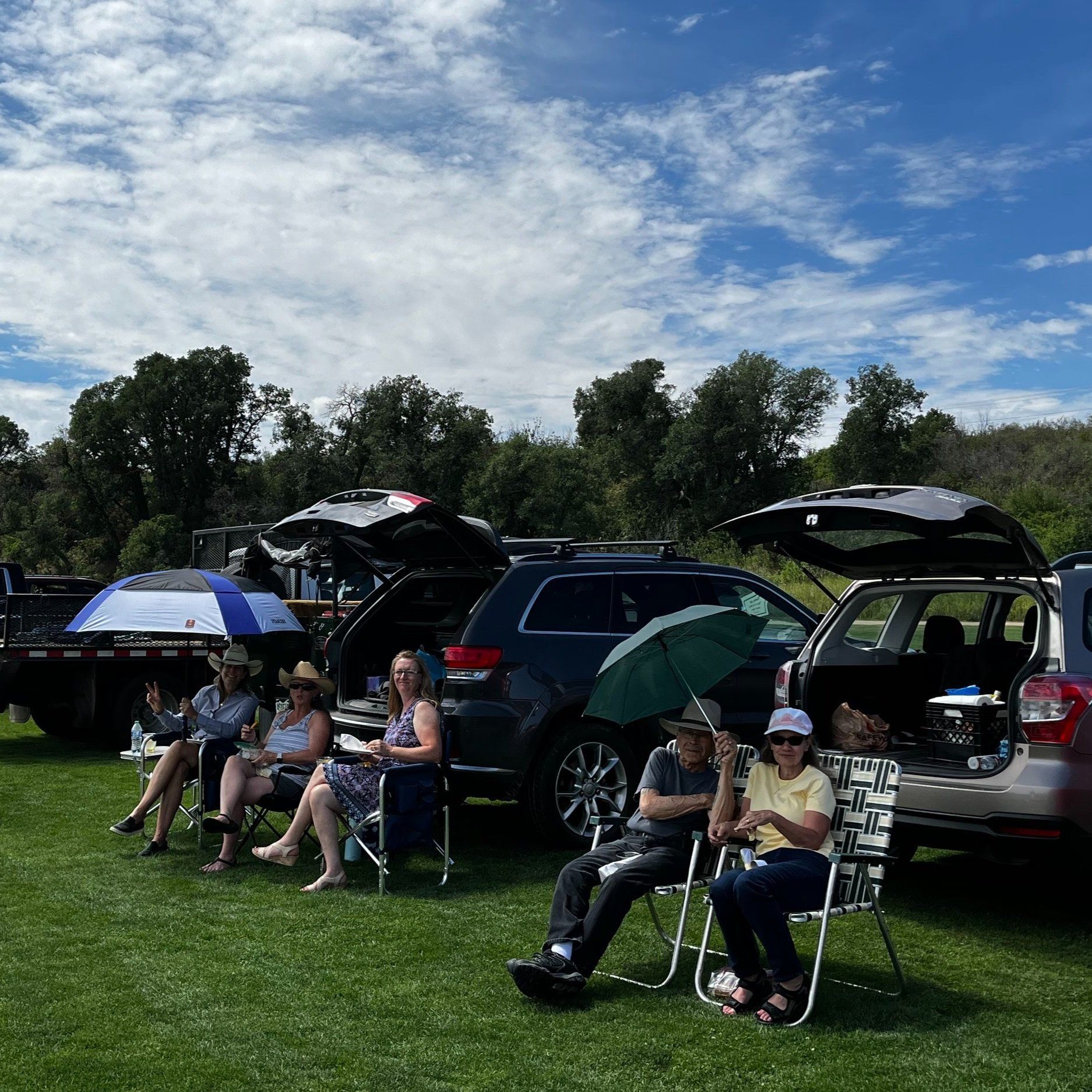 A group of people are sitting in chairs in front of cars.