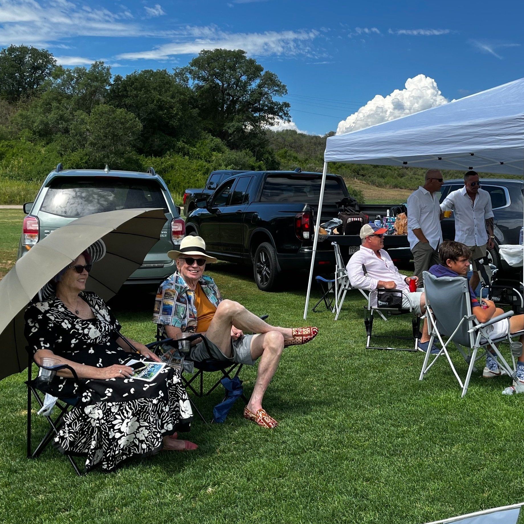 A group of people are sitting under an umbrella in a field