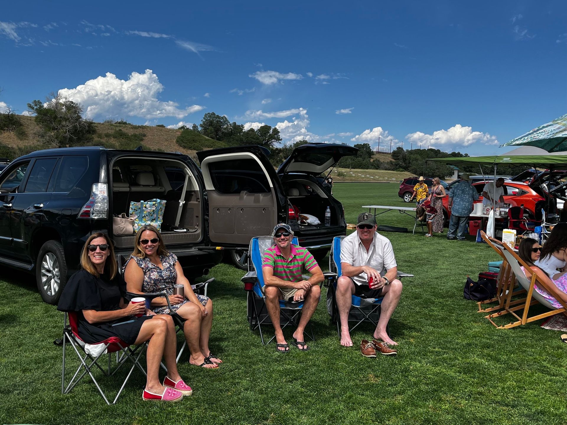 A group of people are sitting in chairs in a field next to a car.