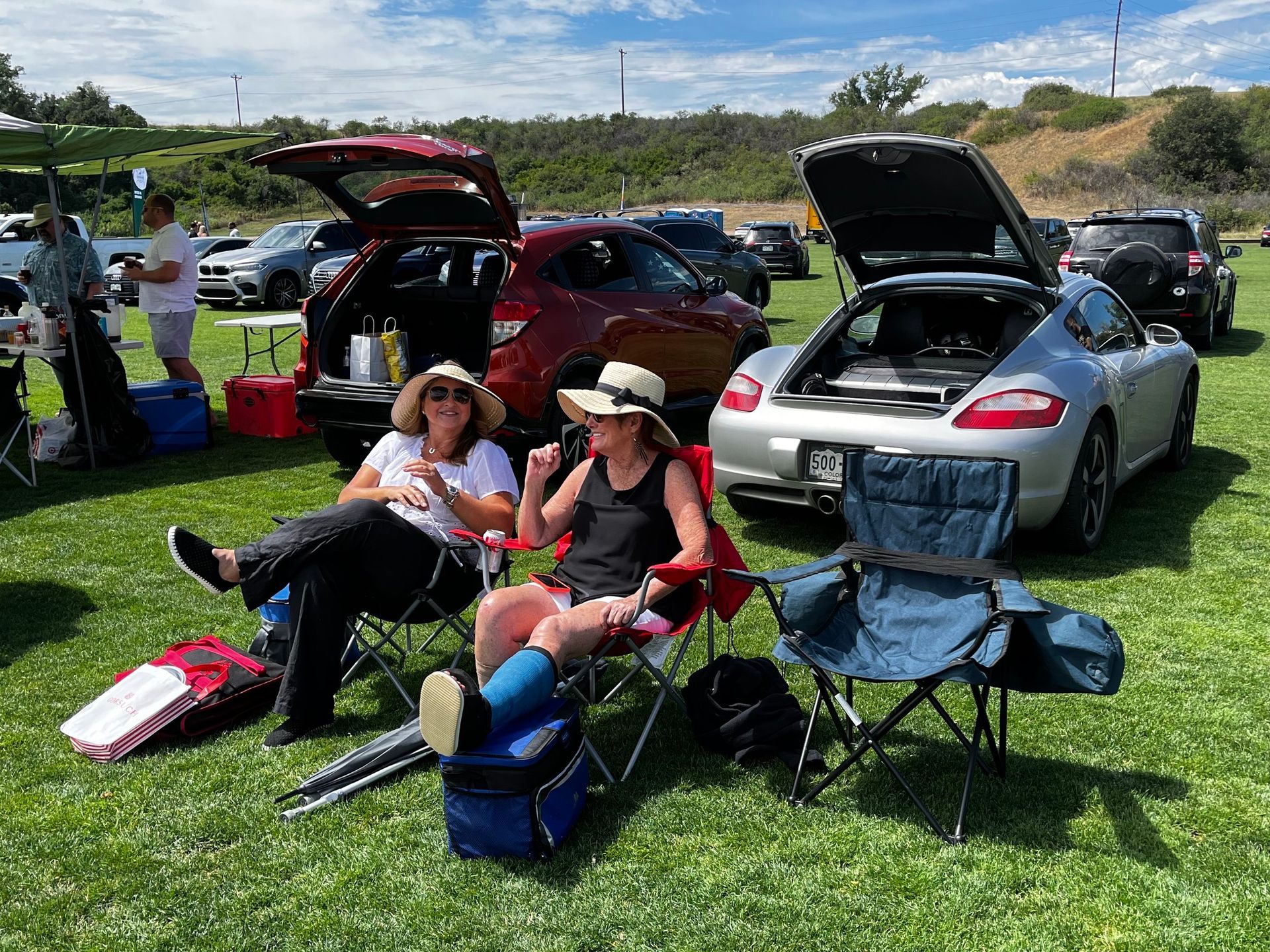 Two women are sitting in chairs in front of a car with the trunk open.