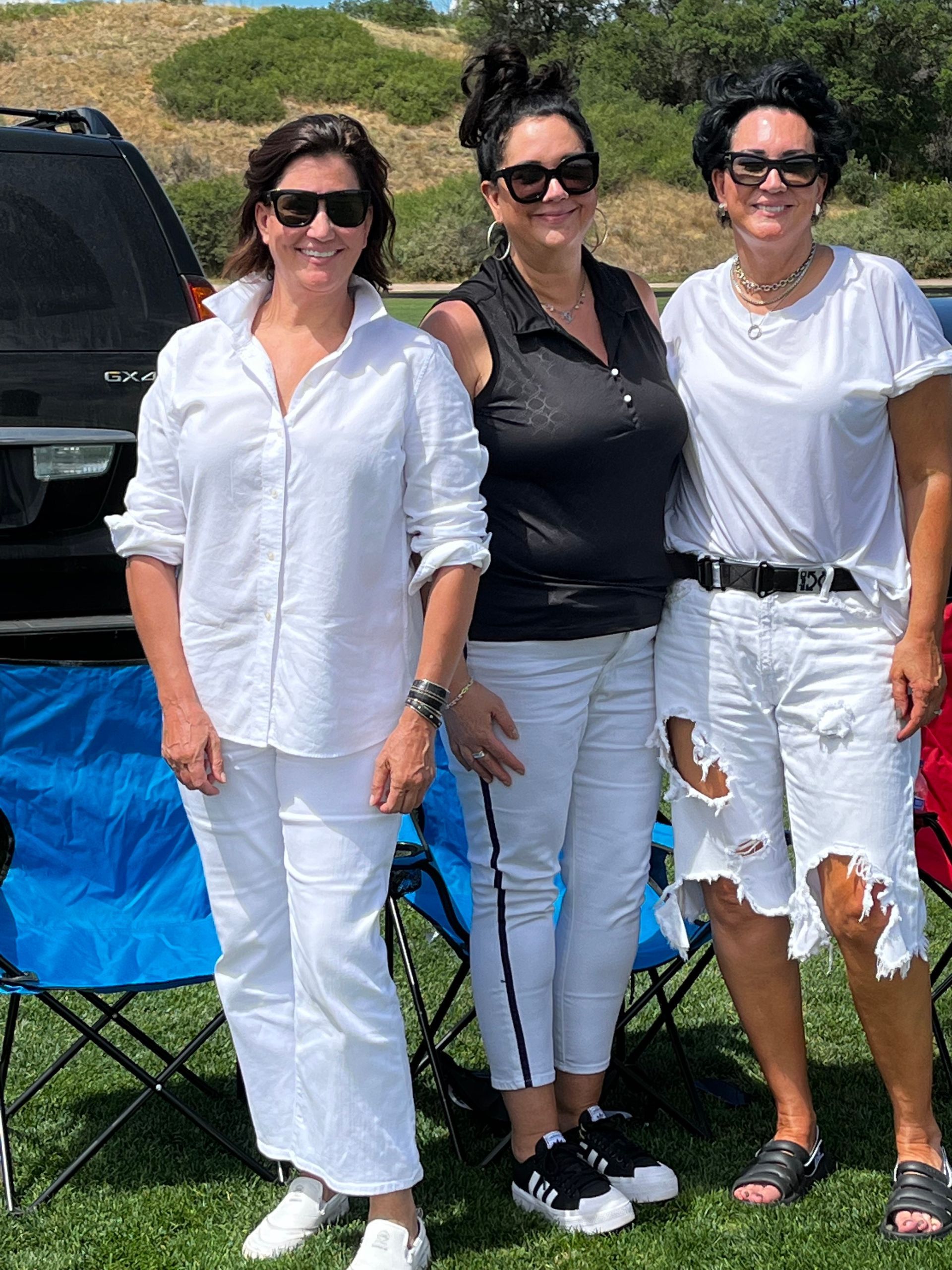Three women wearing white clothes and sunglasses are posing for a picture.