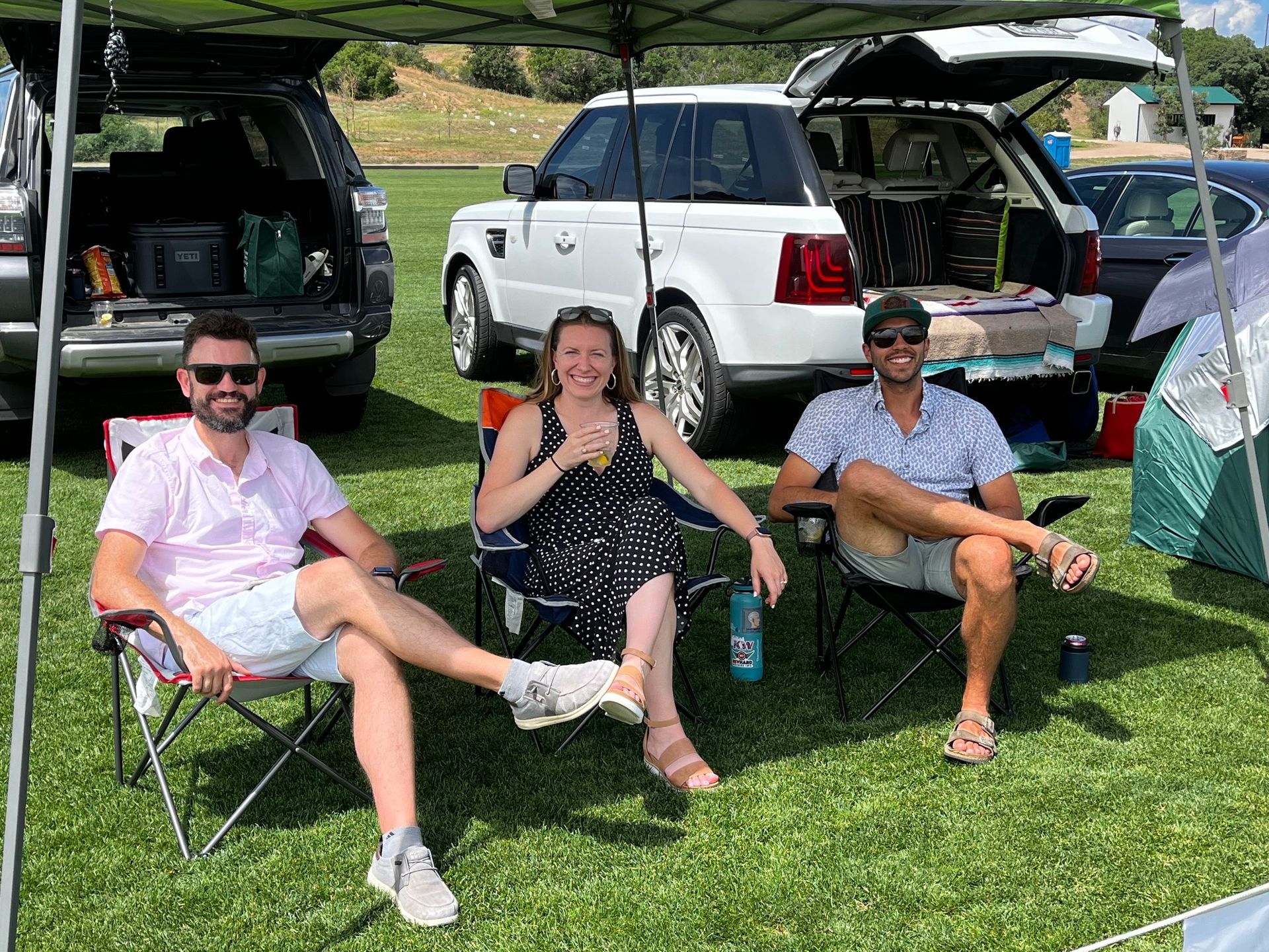 A group of people are sitting under an umbrella in a field.