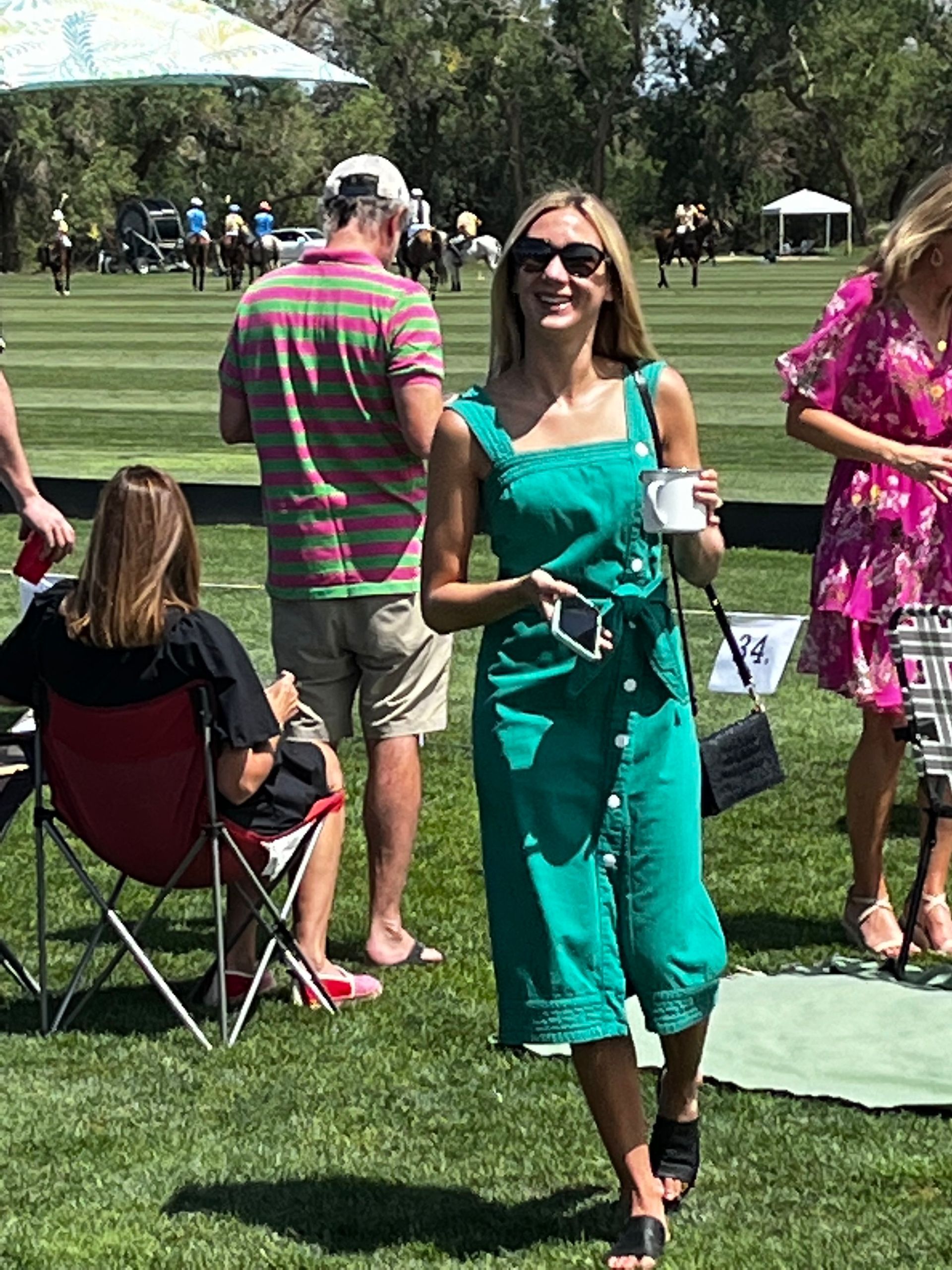 A woman in a green dress is standing in the grass at a polo match.