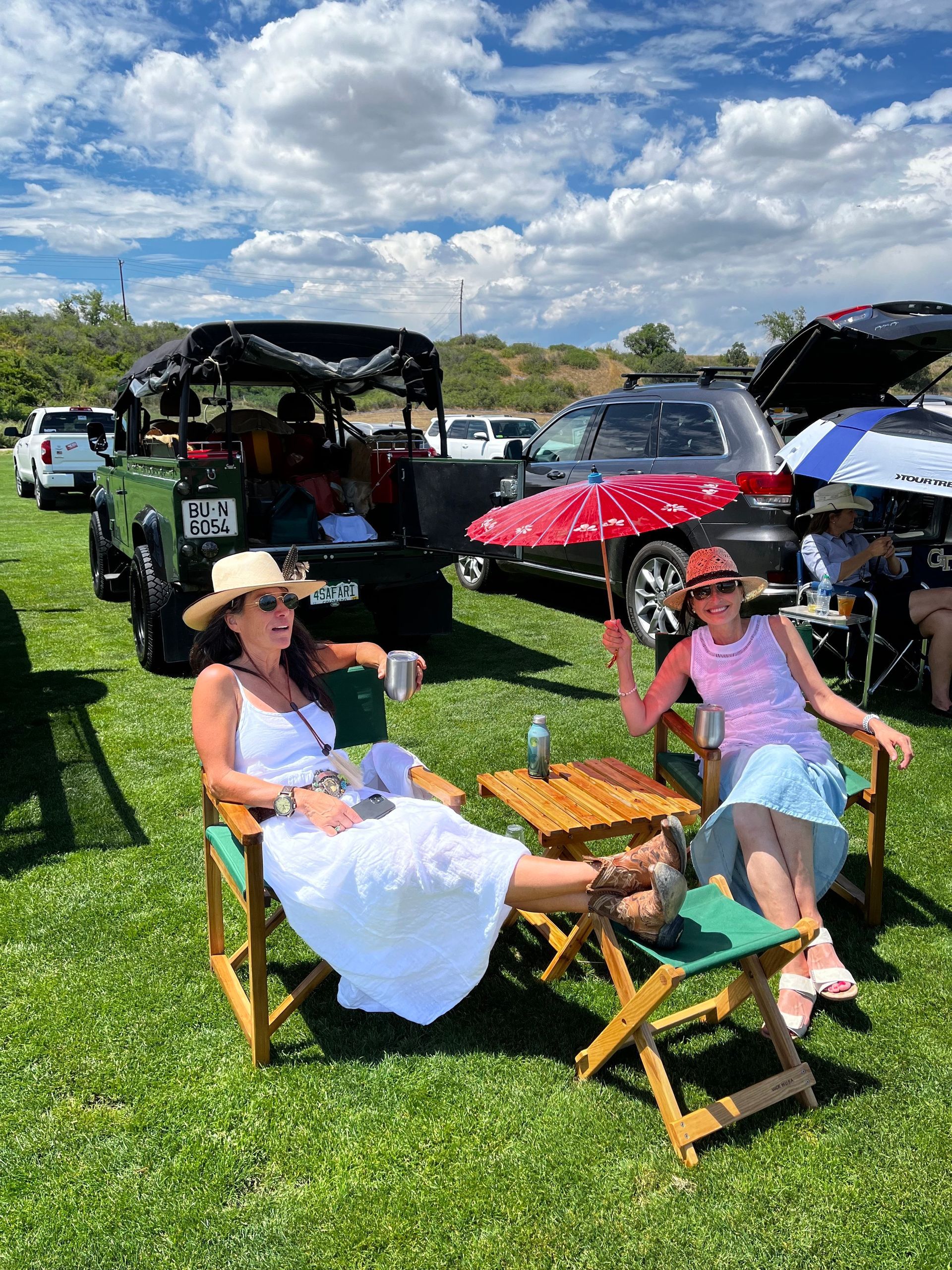 Two women are sitting in folding chairs in a grassy field.