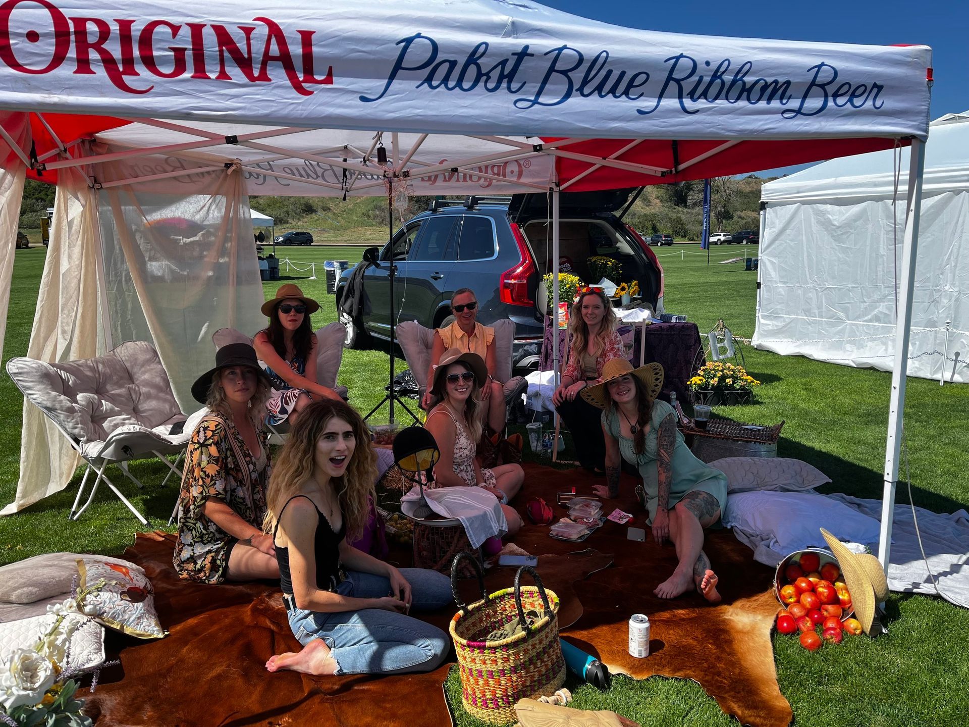 A group of women are sitting under a tent in a field.