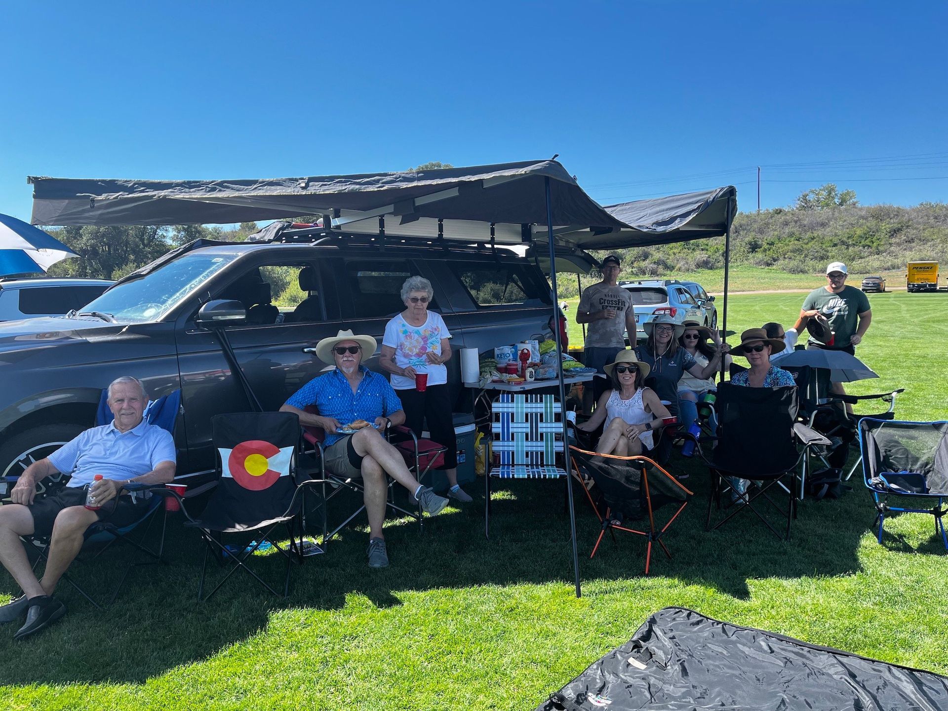 A group of people are sitting in chairs in front of a car.