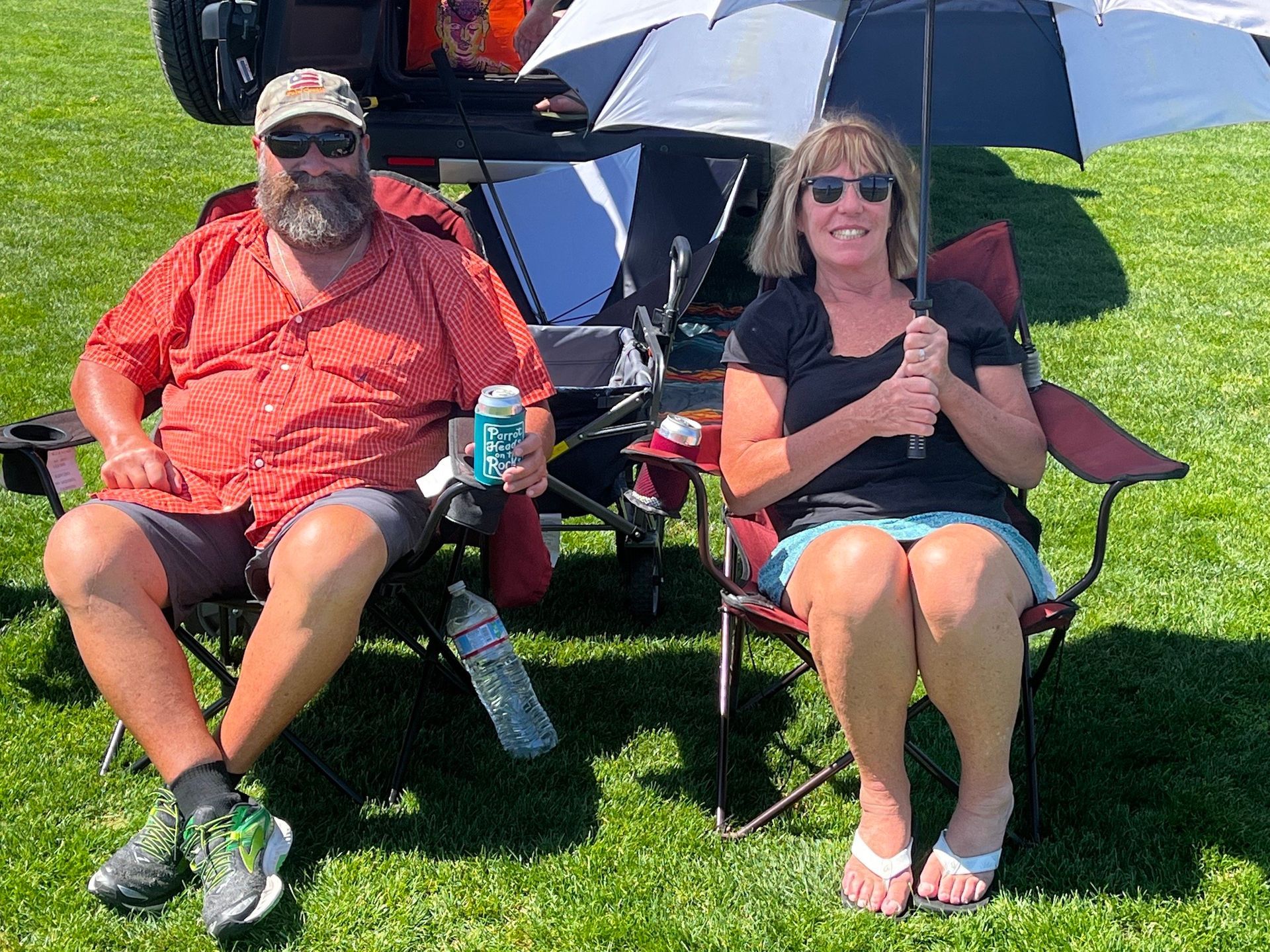 A man and a woman are sitting in chairs in the grass holding umbrellas.