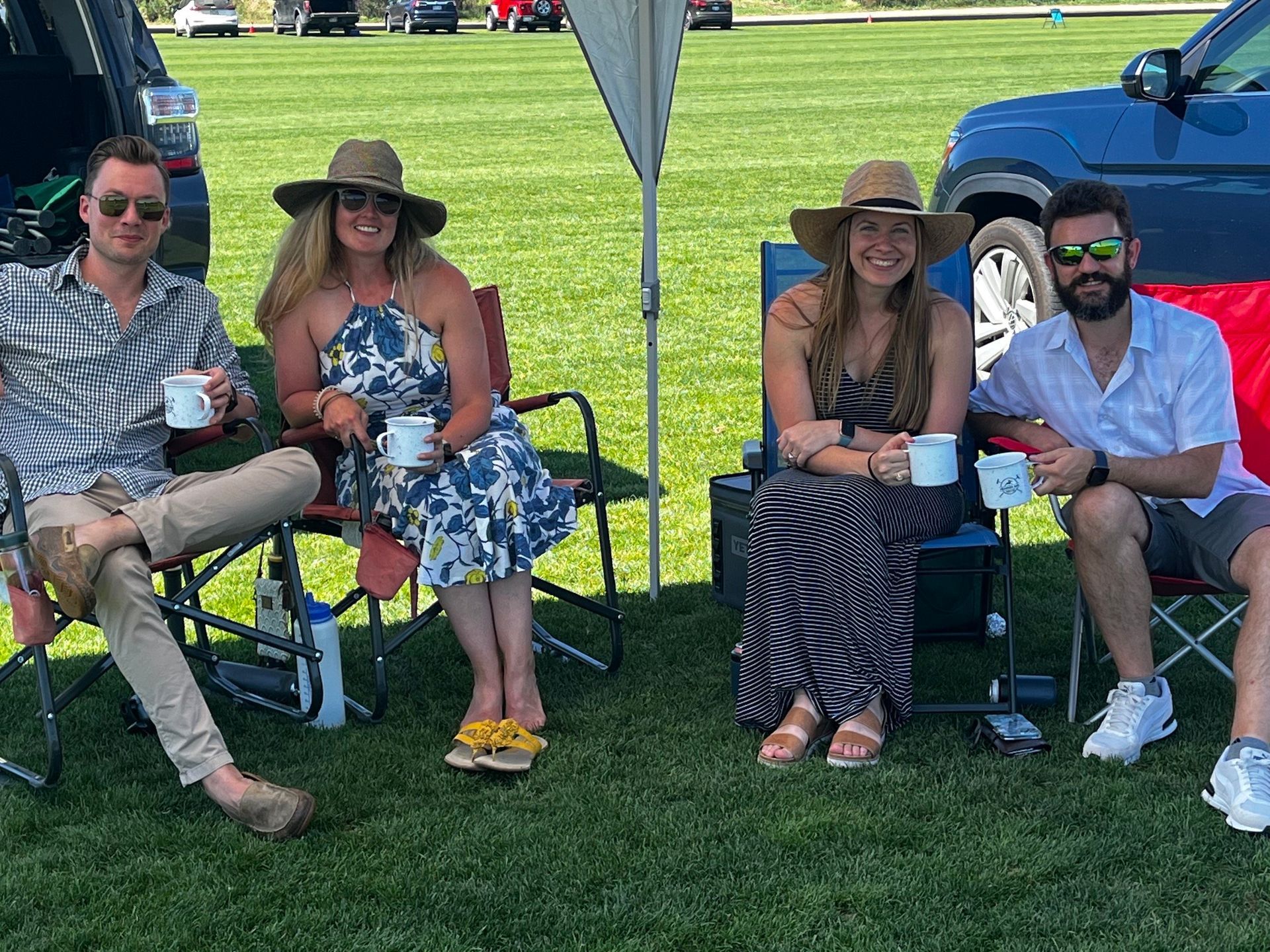 A group of people are sitting in chairs in a field holding cups of coffee.