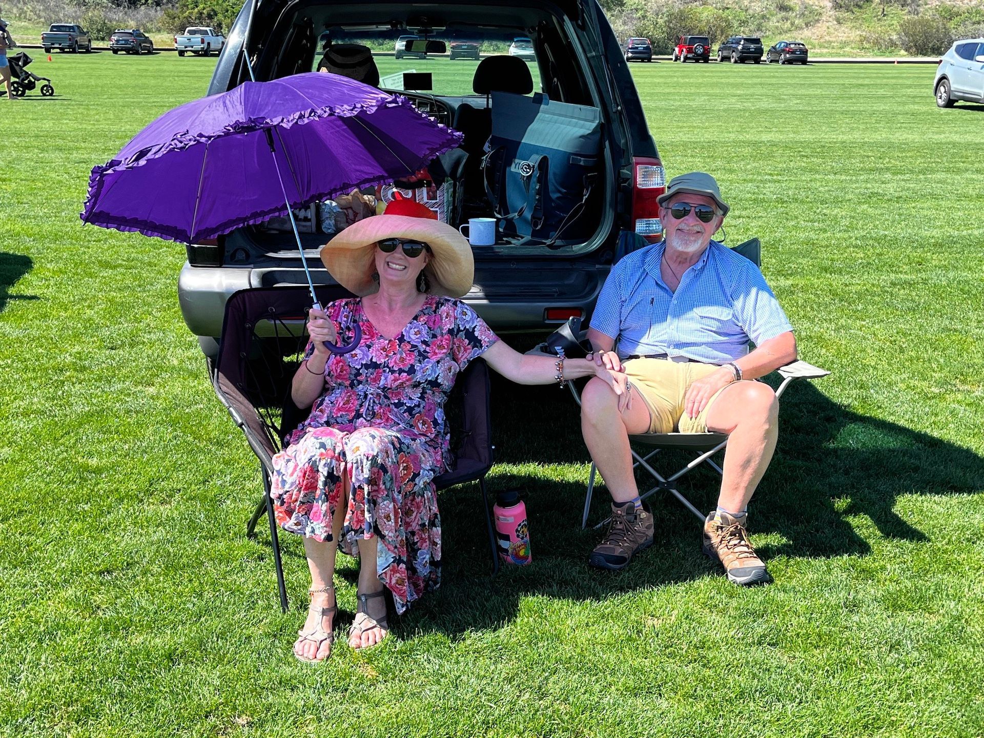 A man and a woman are sitting in front of a car holding umbrellas.