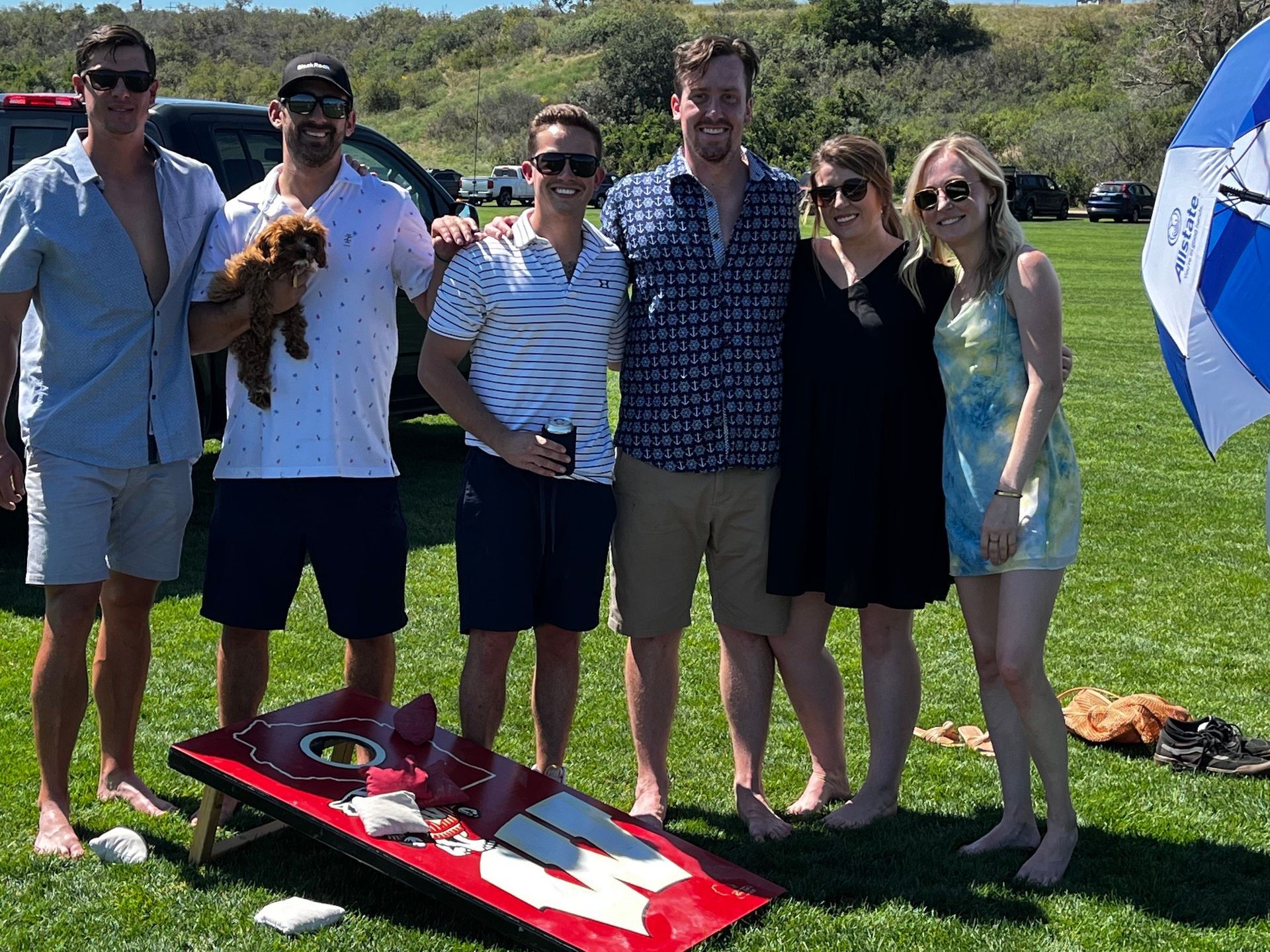 A group of people are posing for a picture in front of a cornhole board.