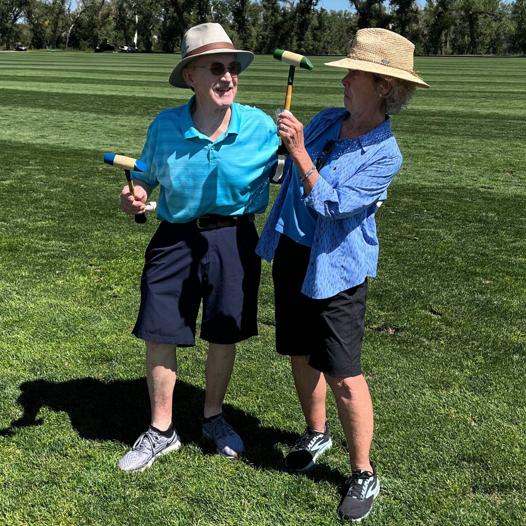 A man and a woman are standing in the grass holding croquet mallets.