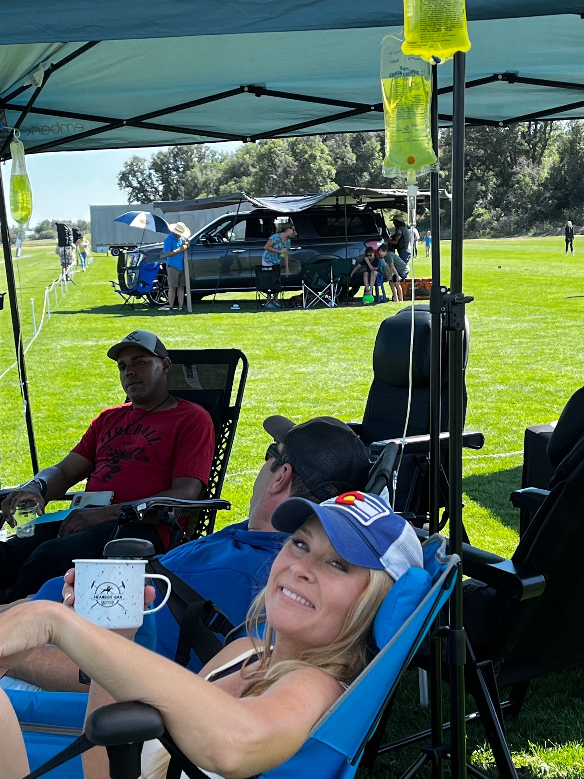 A group of people are sitting under a tent in a field.