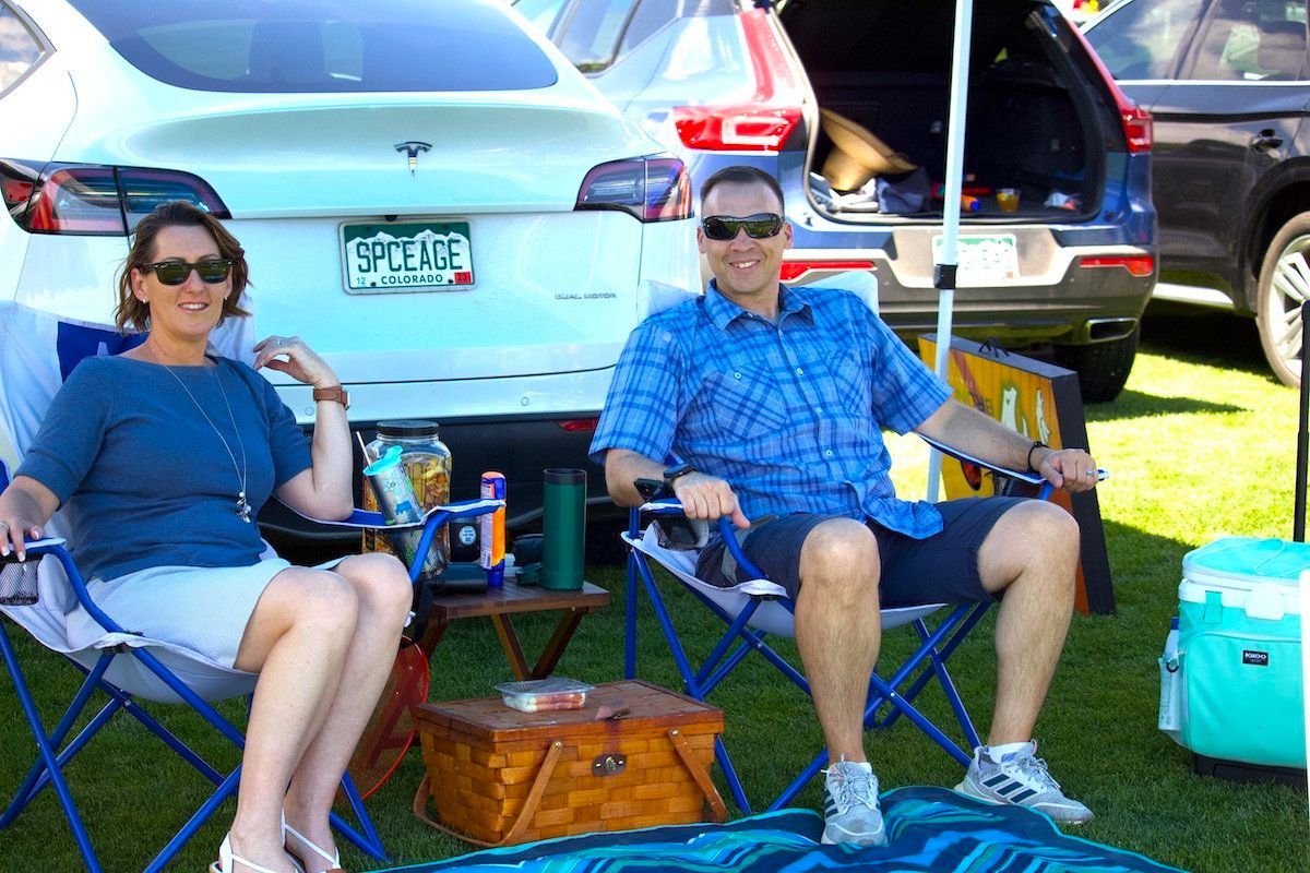 A man and a woman are sitting in folding chairs in front of a car.