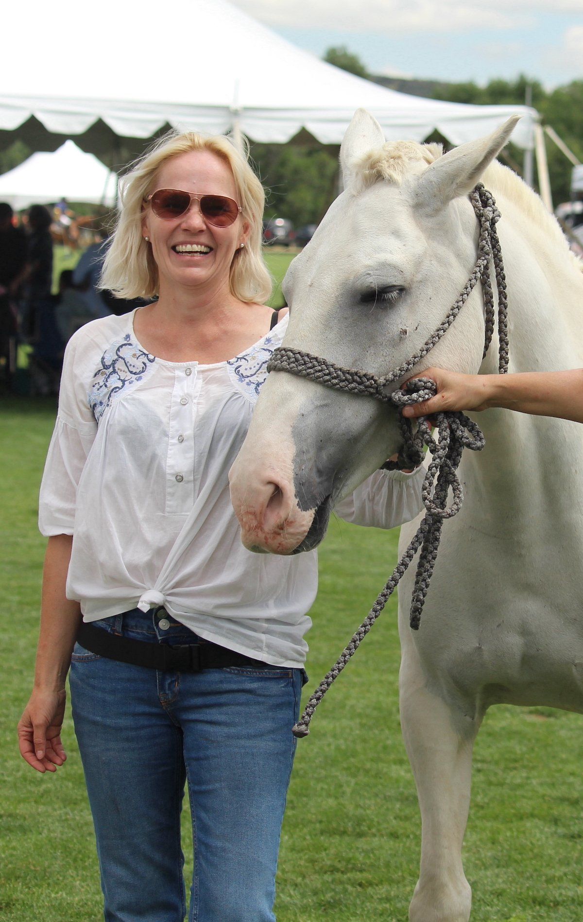 A woman is standing next to a white horse in a field.