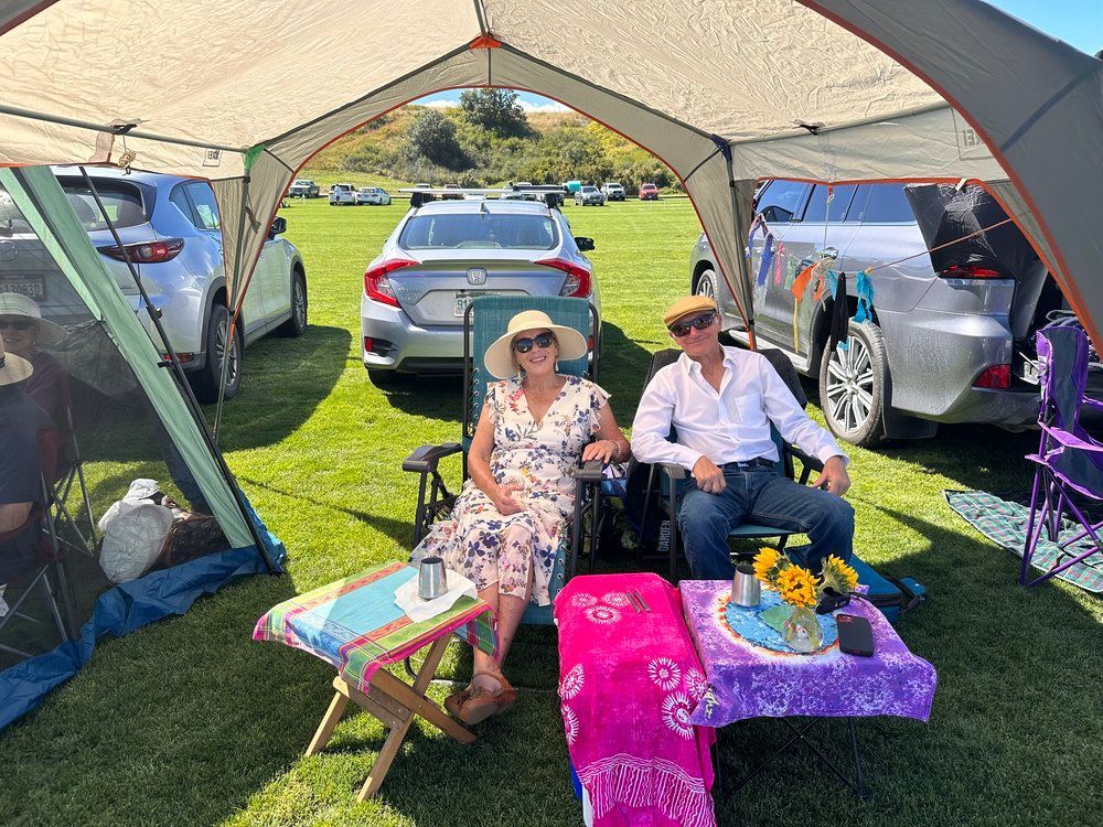 A man and a woman are sitting under a tent in a field.