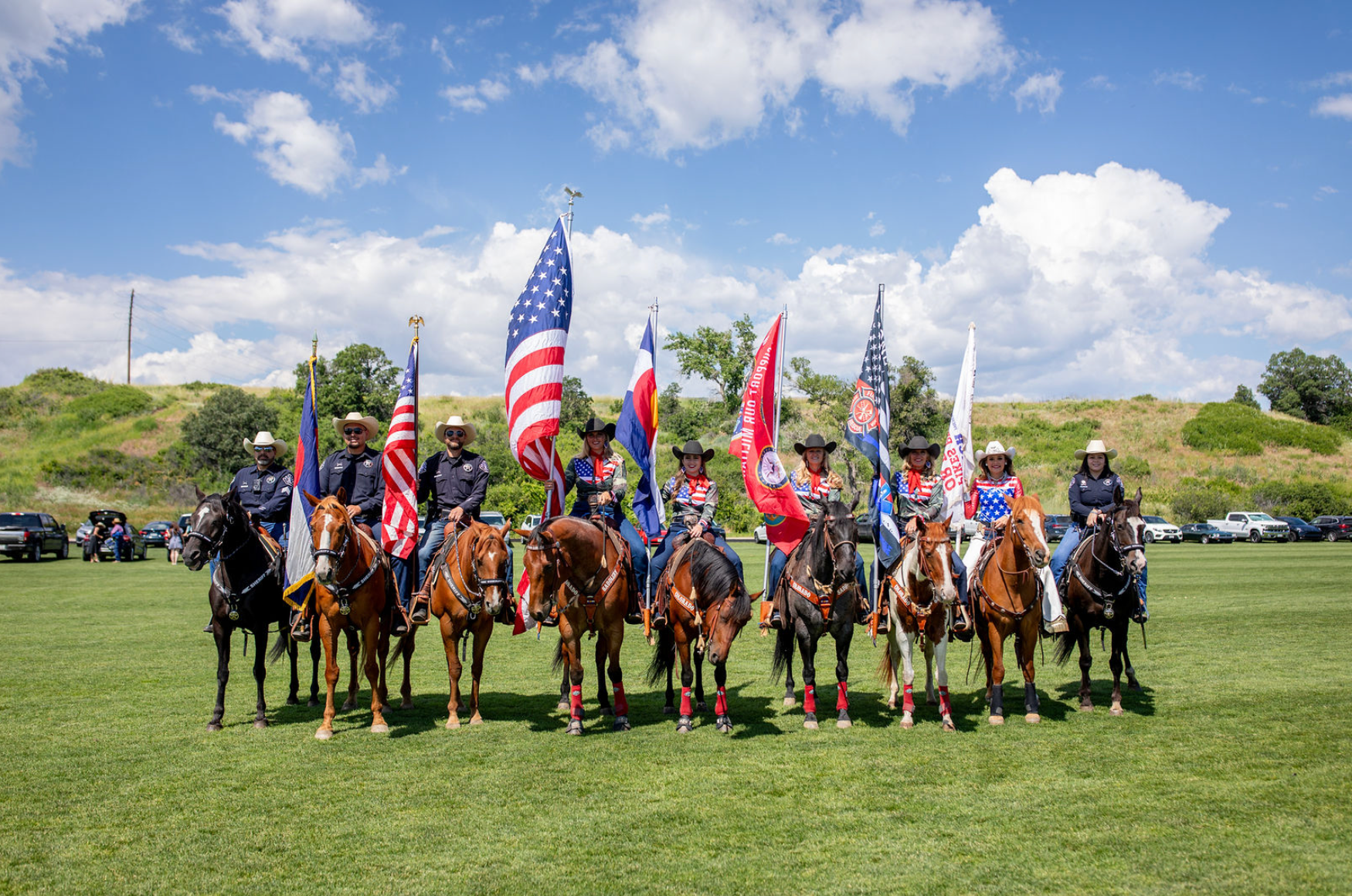 A group of people riding horses in a field holding flags.
