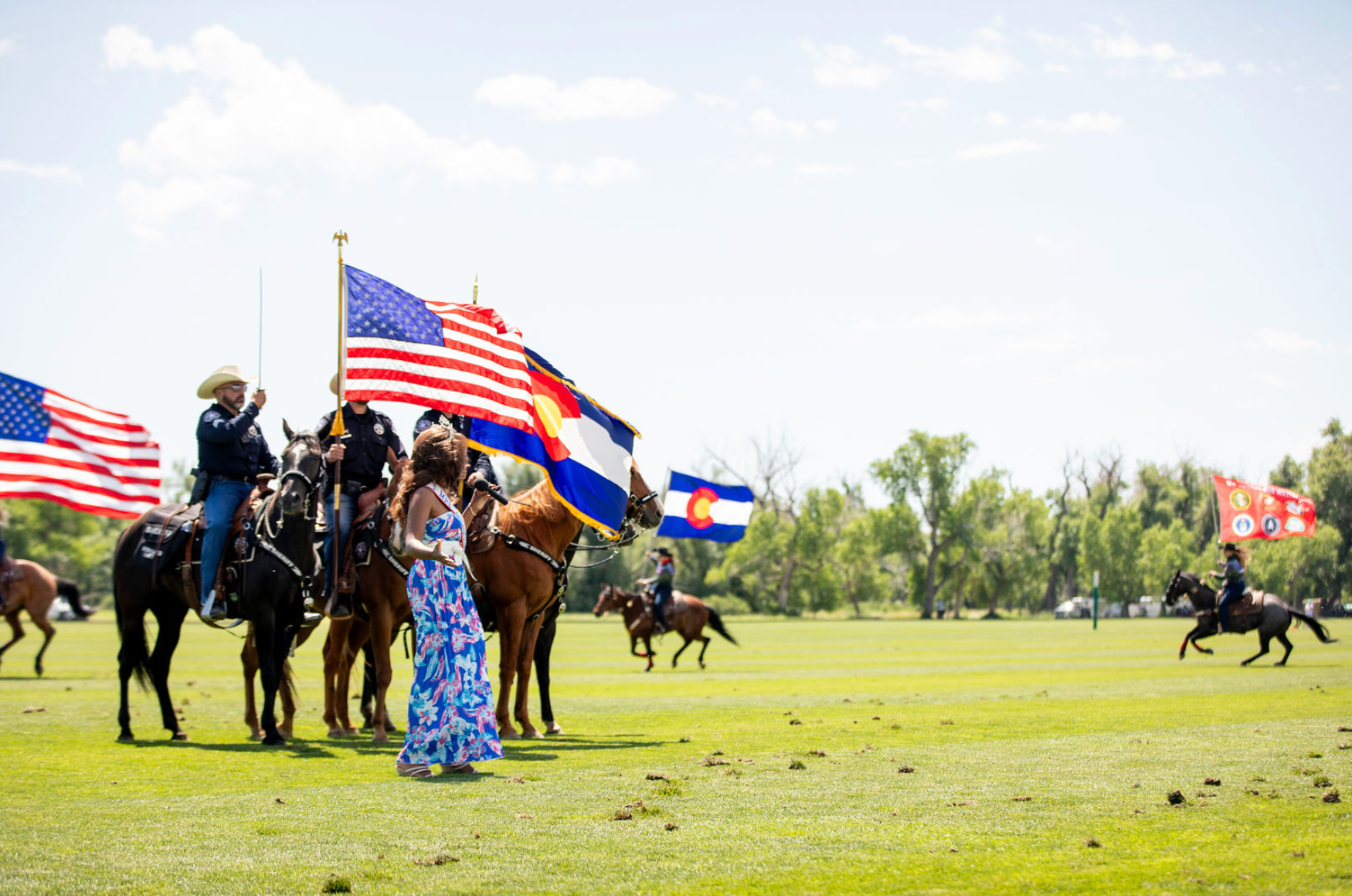 A group of people riding horses holding flags in a field.