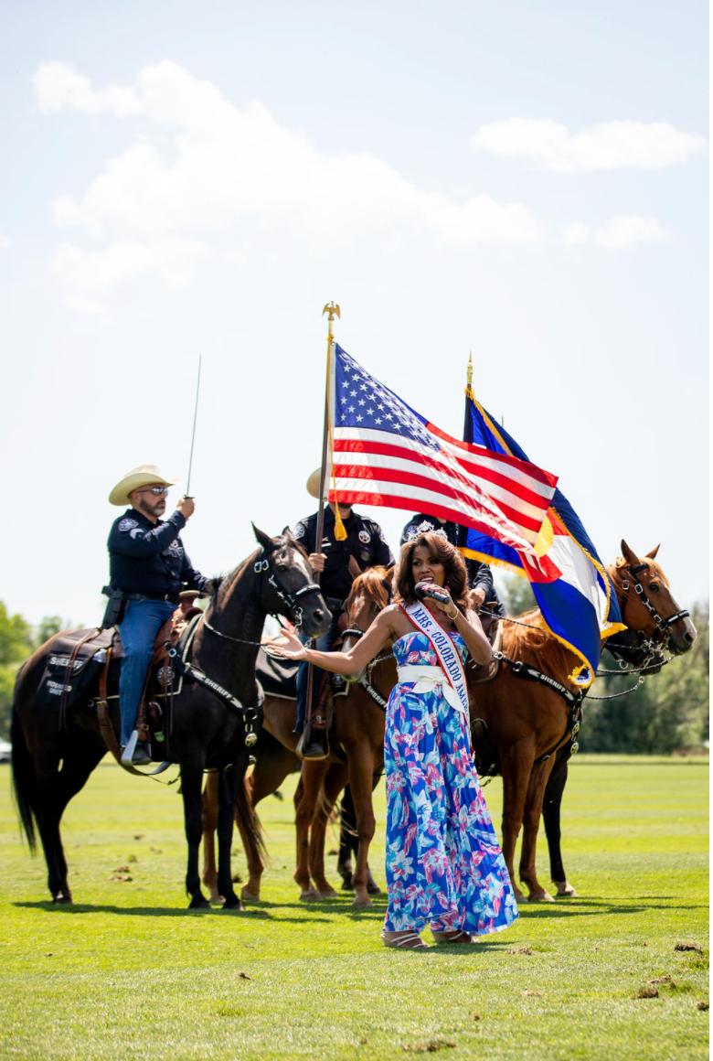 A woman is standing in front of a group of horses holding an american flag.