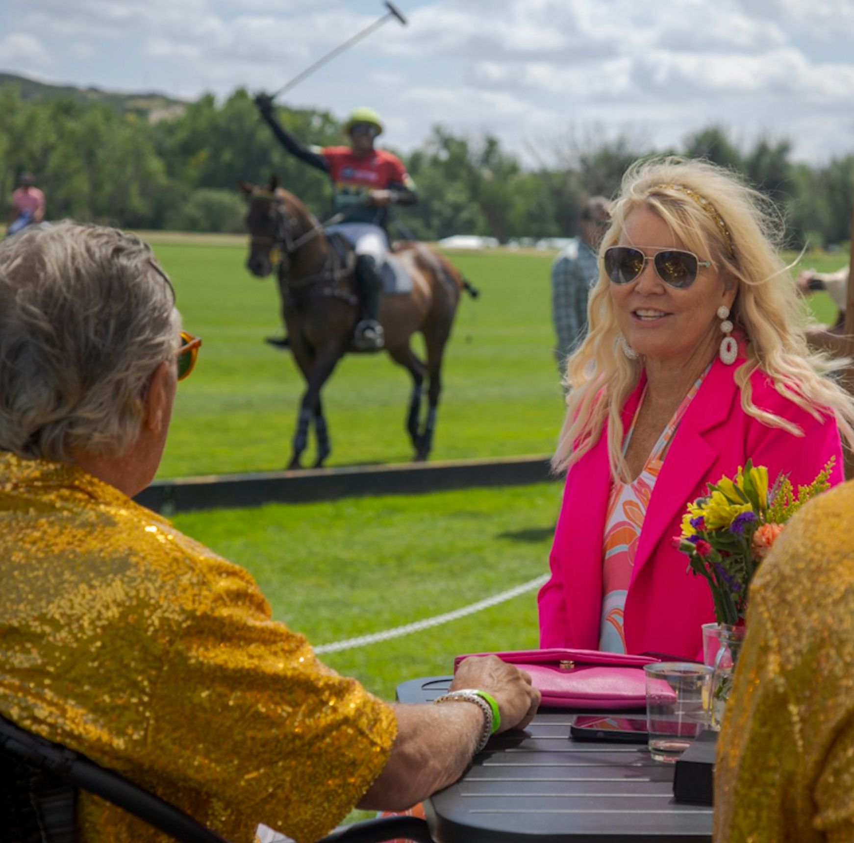 A woman in a pink jacket is sitting at a table watching a man on a horse