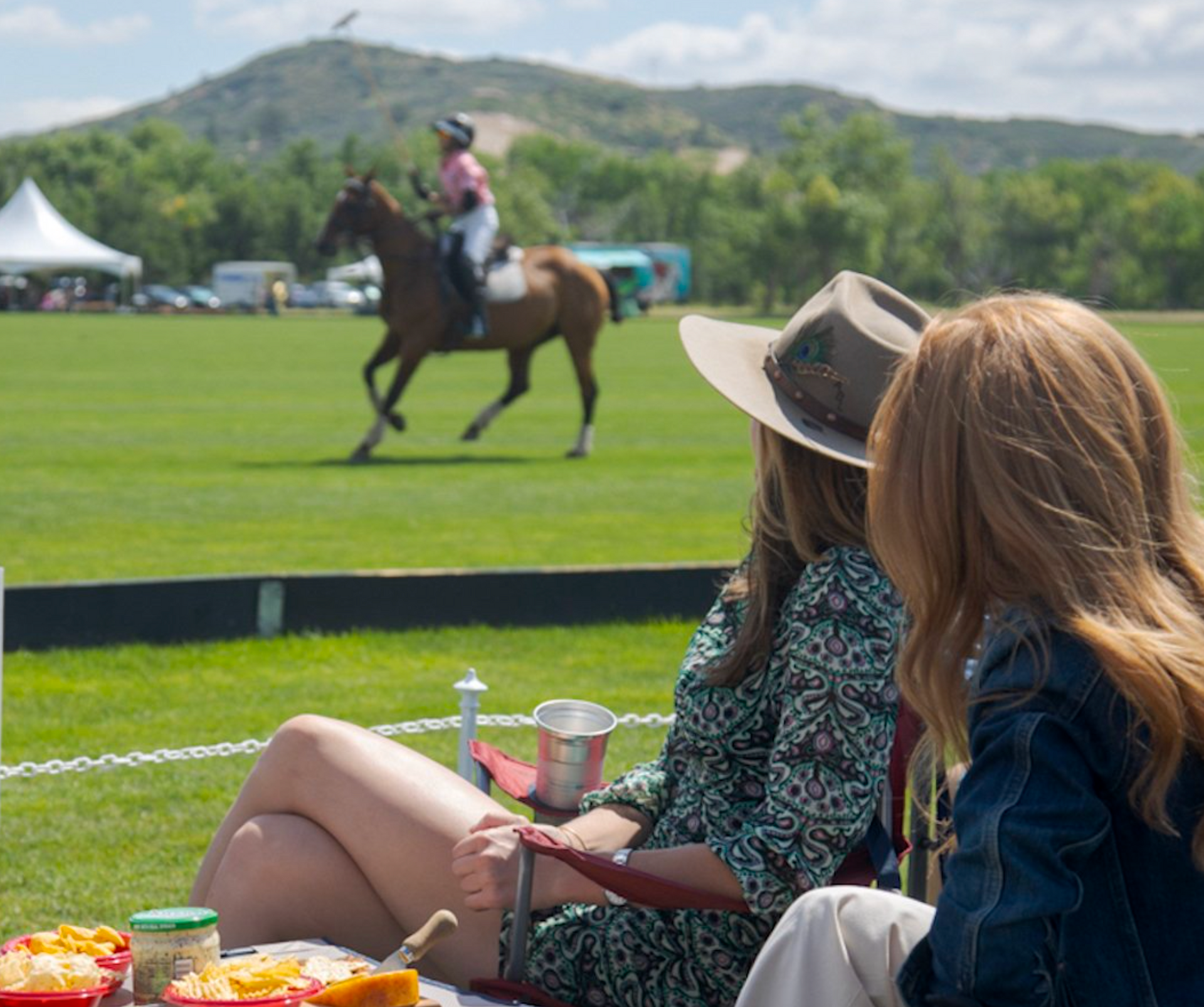 Two women sitting on the grass watching a horse race