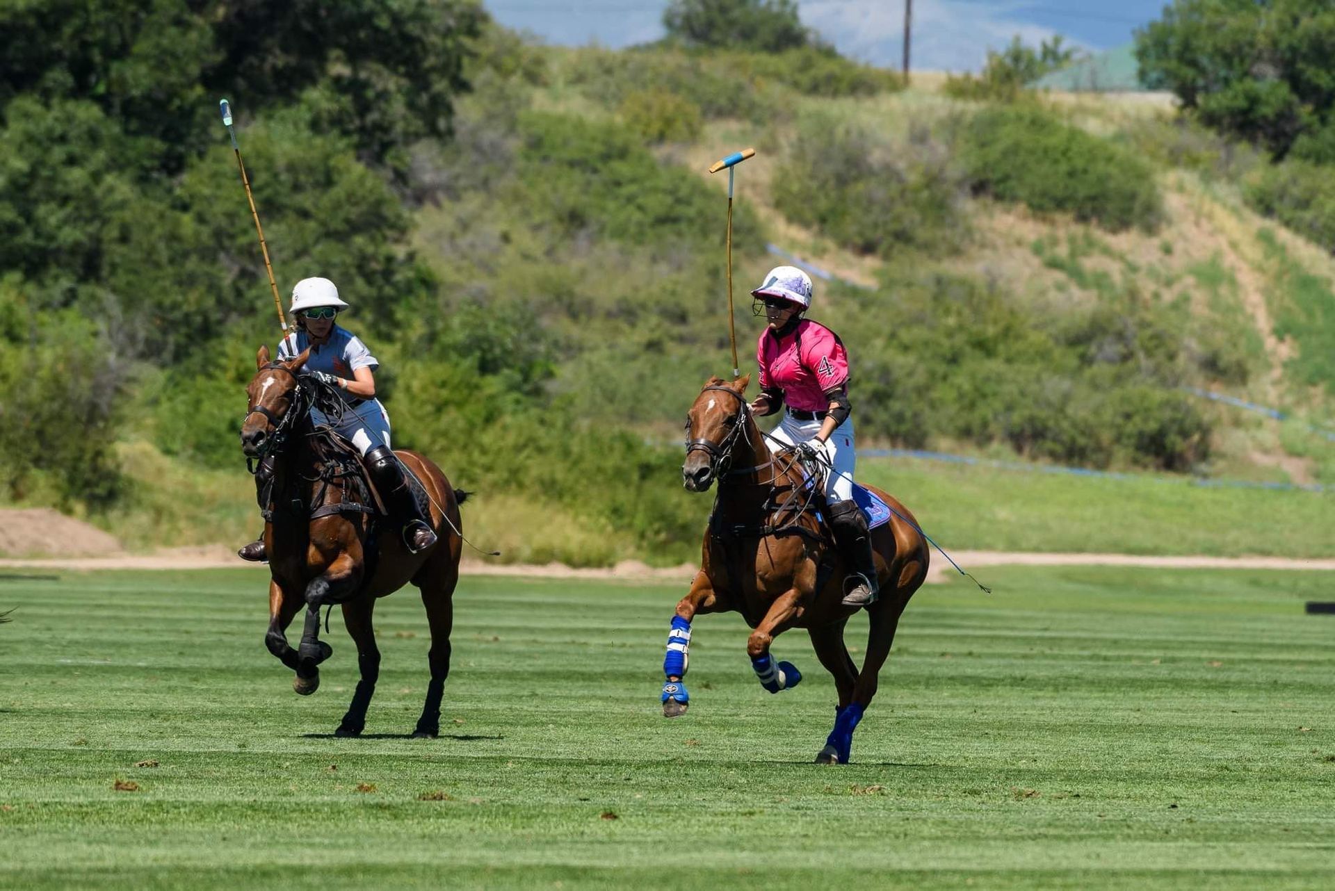 Two people are riding horses on a field while playing polo.