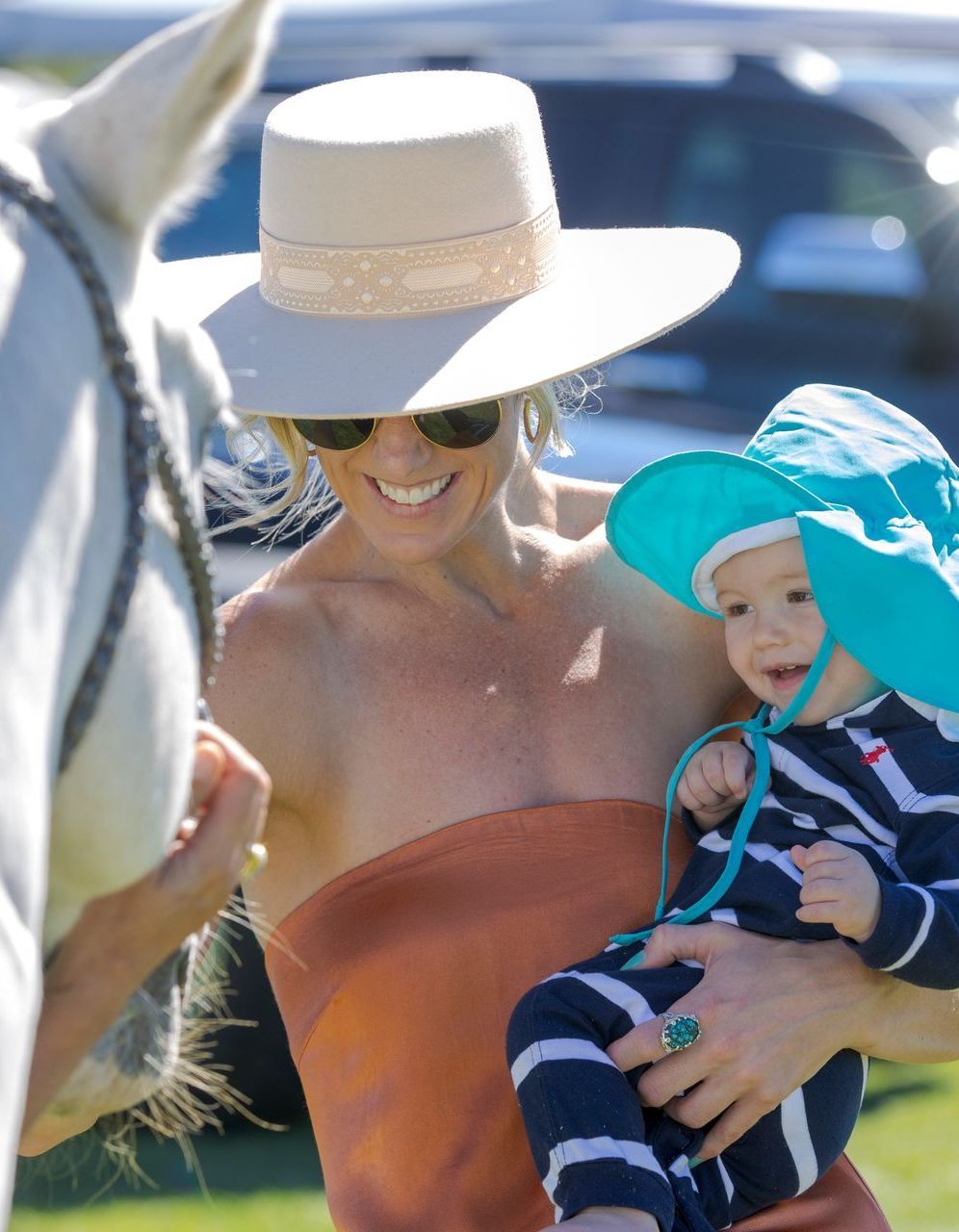 A woman in a hat is holding a baby in front of a horse