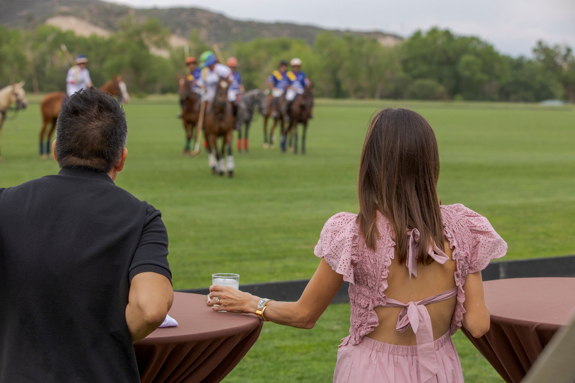 A man and a woman are watching a polo match on a field.