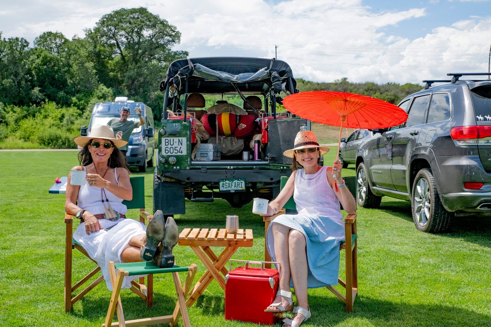 Two women are sitting in folding chairs in front of a car.