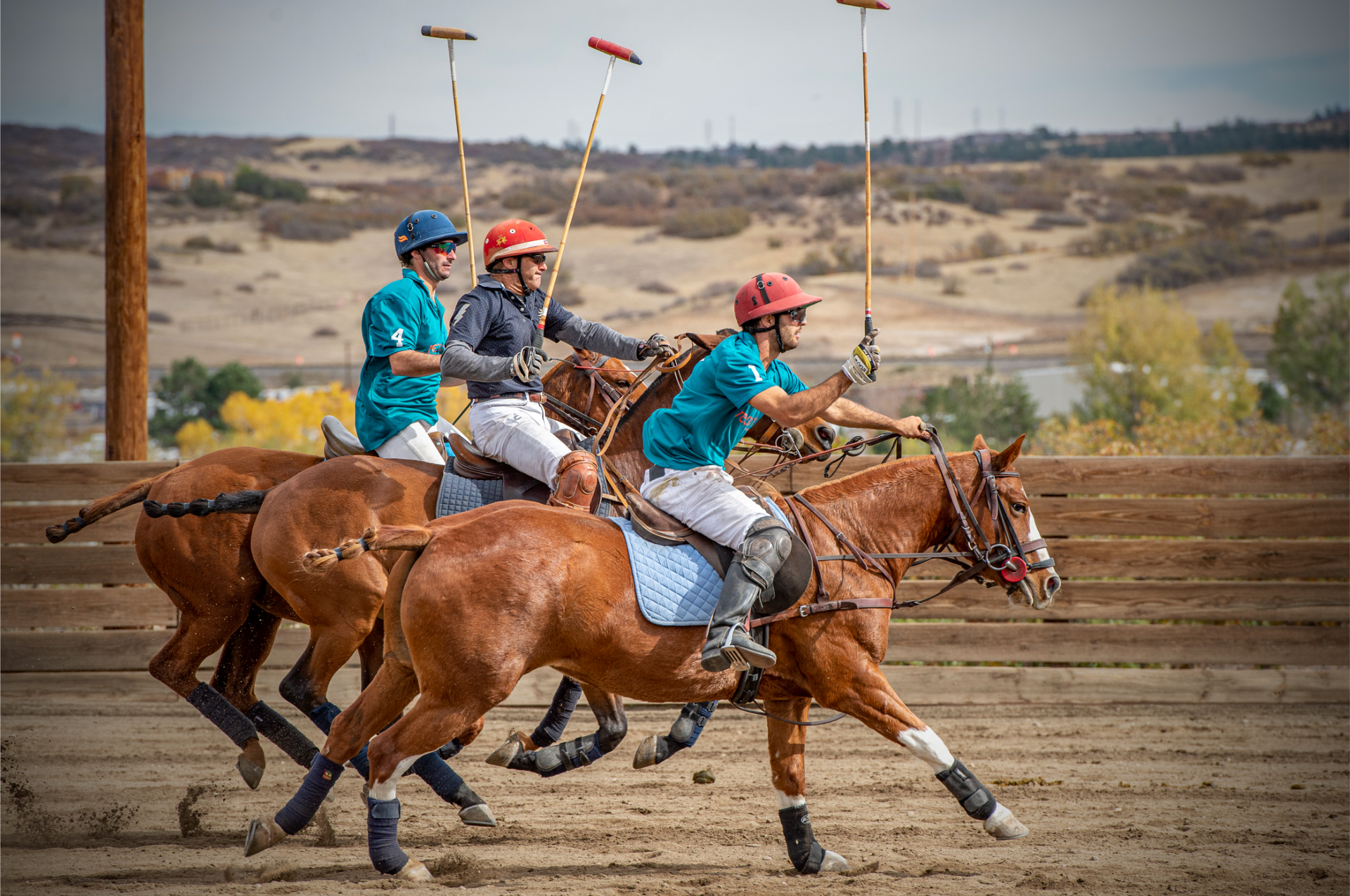 A group of people are riding horses and playing polo on a dirt field.