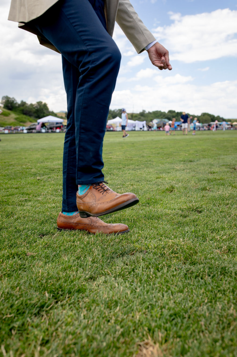 A person wearing brown shoes is standing on a lush green field.