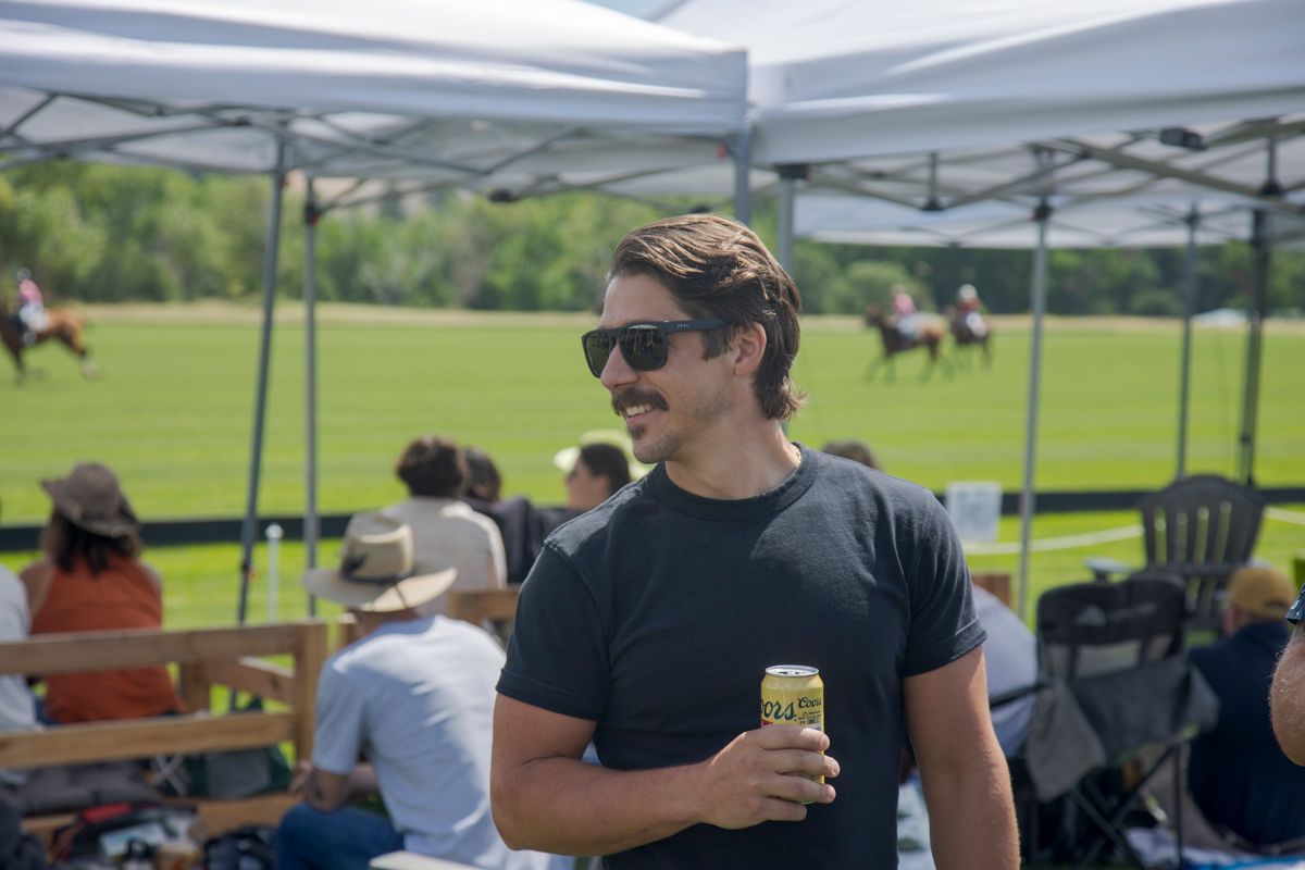 A man is standing in front of a tent holding a can of beer.