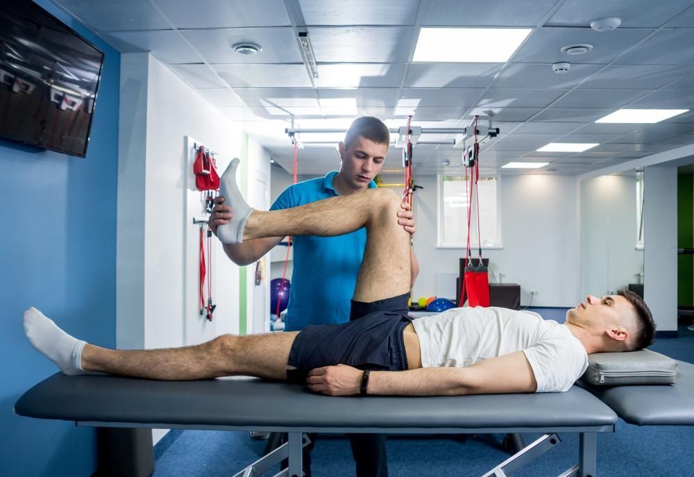 A Man Is Laying on A Table While a Man Stretches His Leg — St Vincents Physiotherapy & Day Rehab in East Lismore, NSW