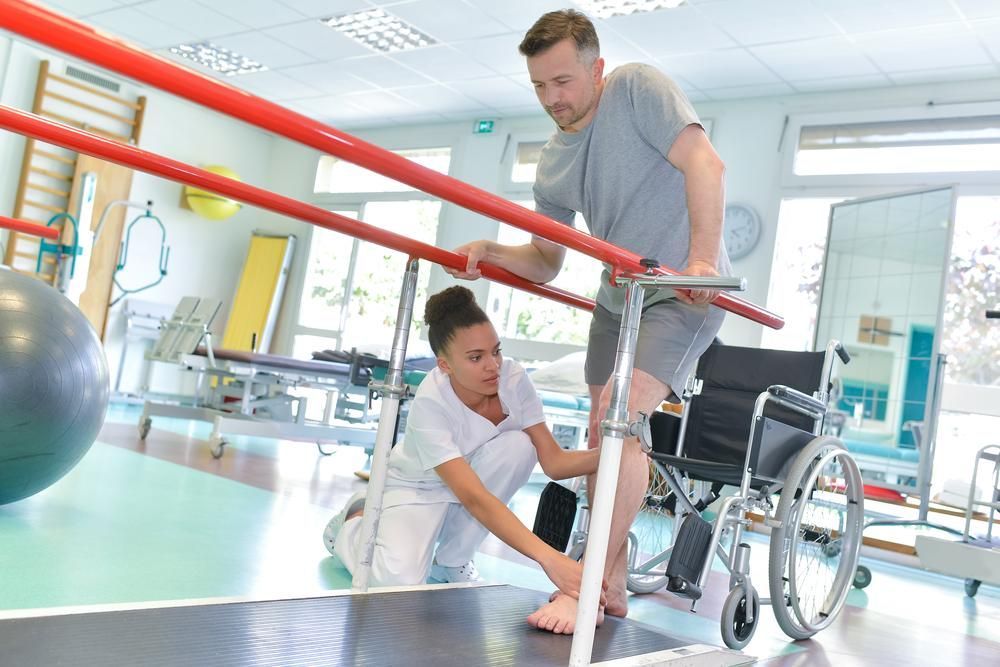 A Man in A Wheelchair Helped by A Nurse to Walk on Parallel Bars — St Vincents Physiotherapy & Day Rehab in East Lismore, NSW