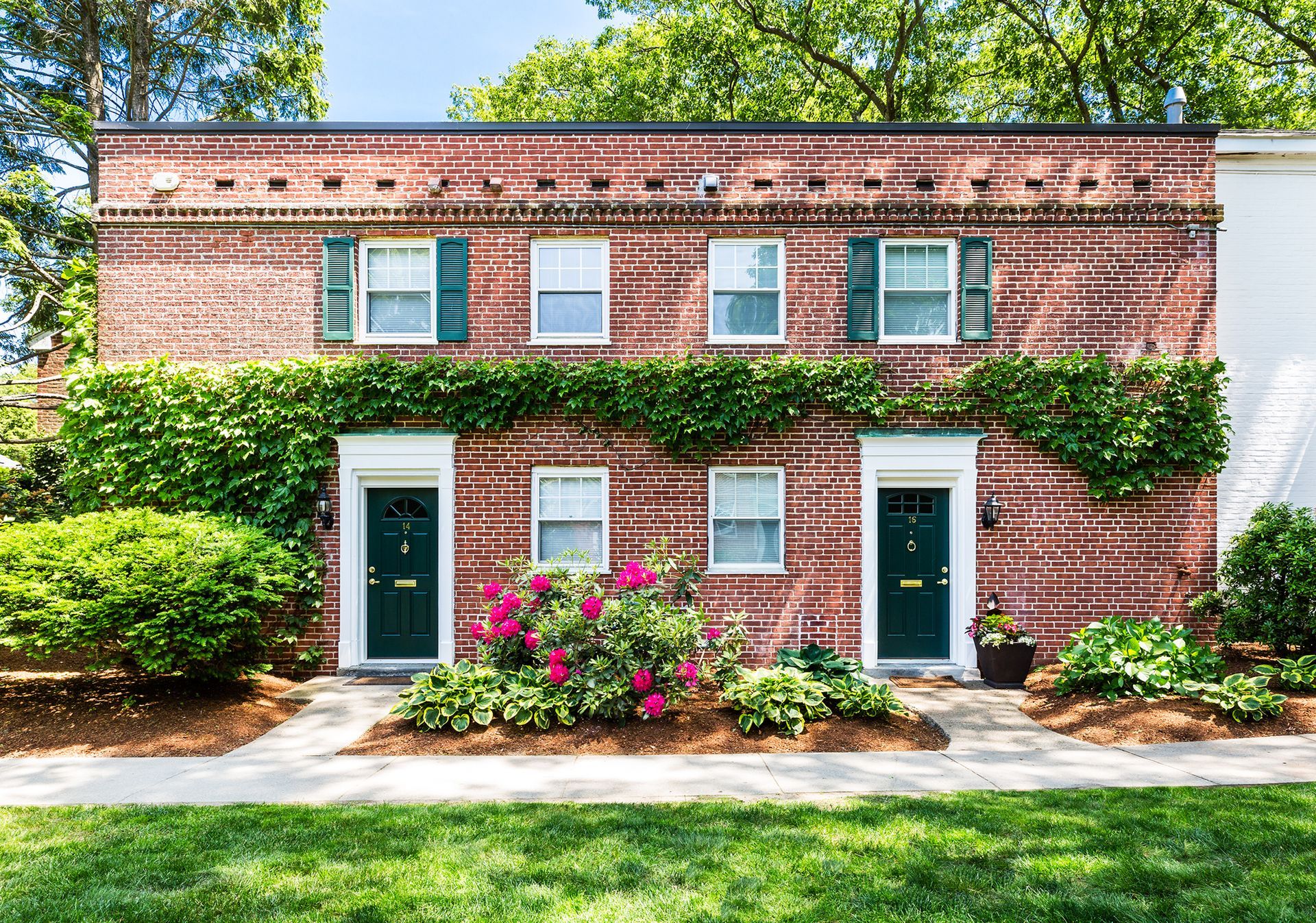 A brick building with green shutters and flowers in front of it.
