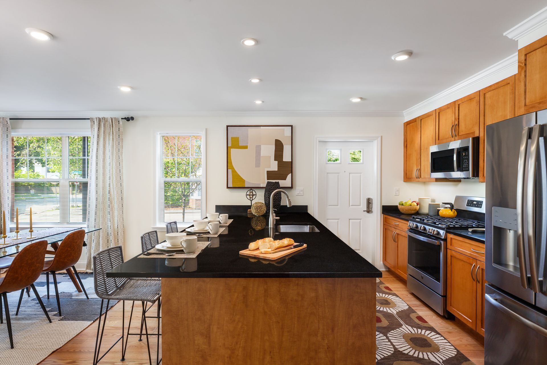 Kitchen with island and stainless steel appliances; wood cabinets, black countertop, open to dining area.