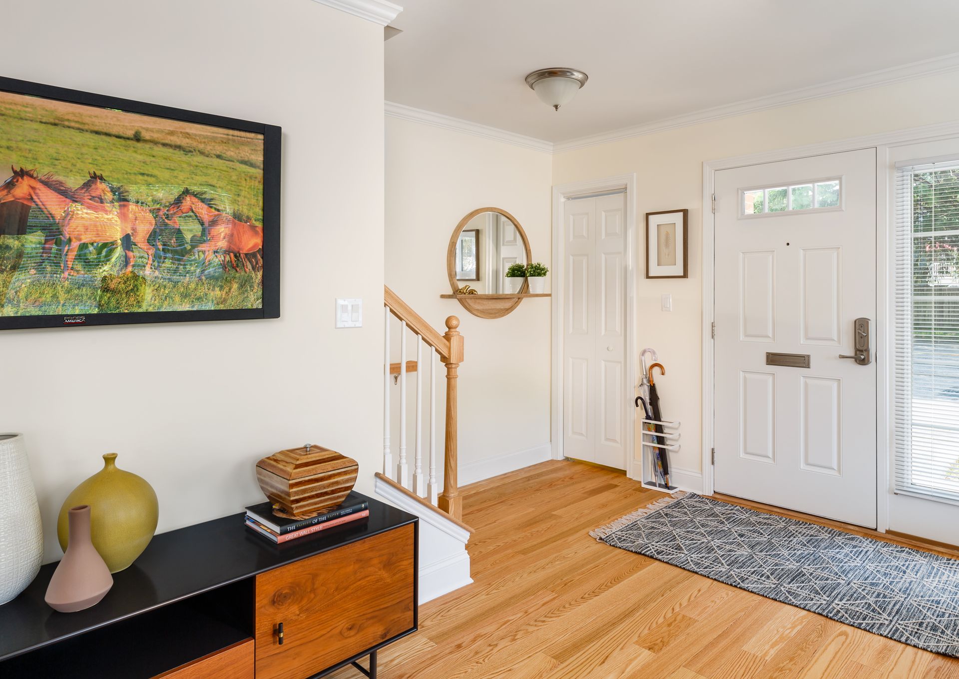 Entryway with hardwood floors, a black console table, and a framed horse painting. White door and walls.