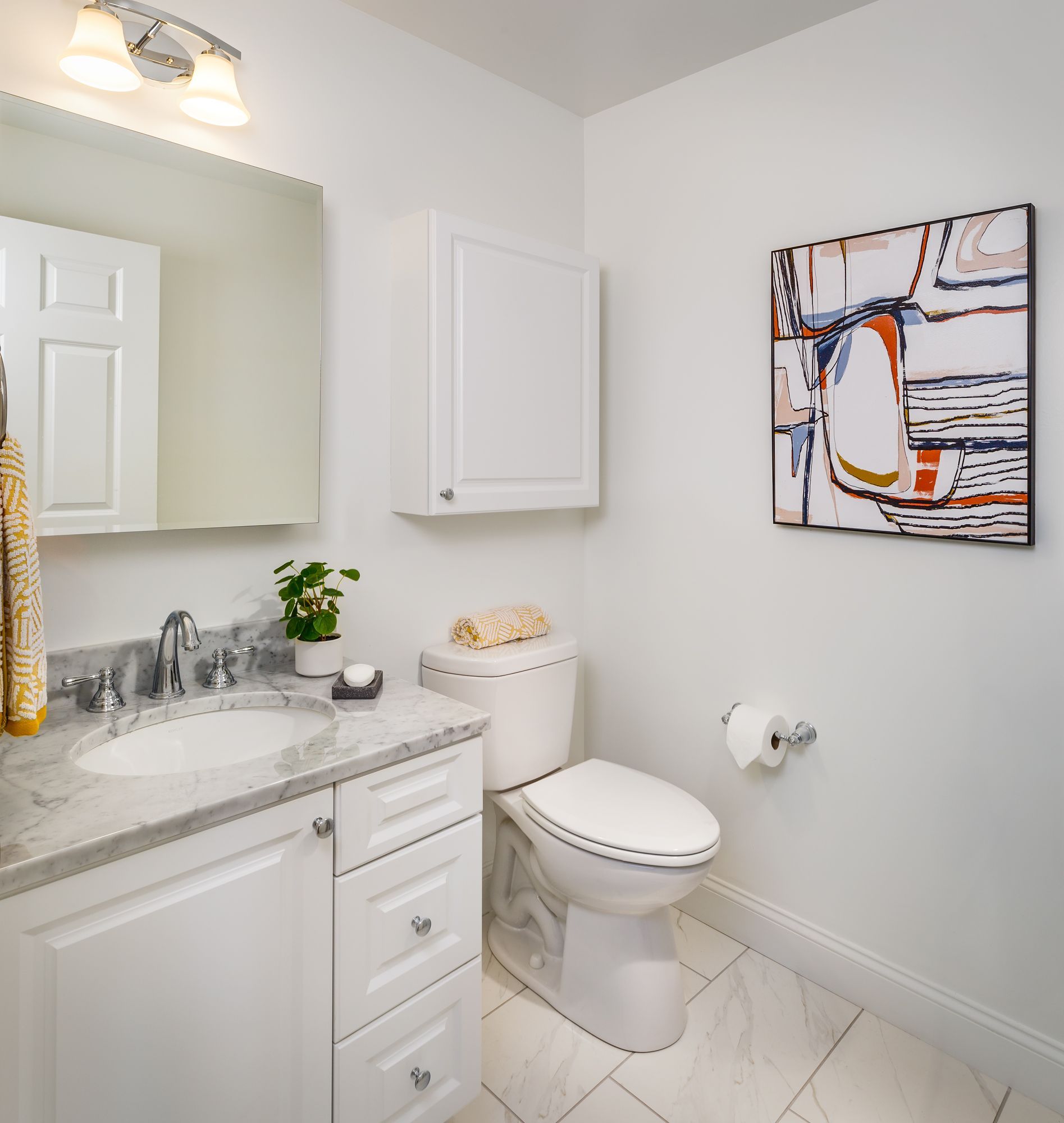 White bathroom with a vanity, toilet, cabinet, and abstract art.