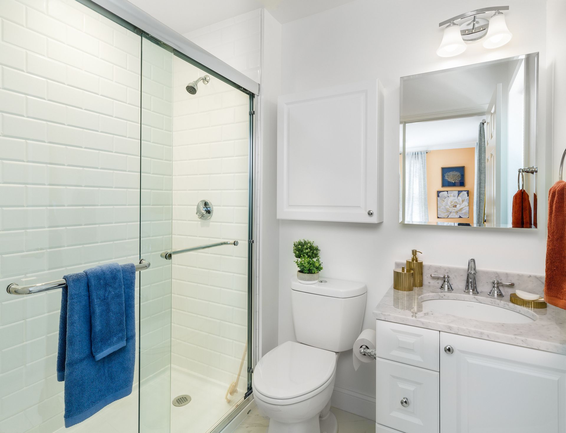 White bathroom with a glass shower, toilet, sink, and cabinet. Blue towel hangs on shower.