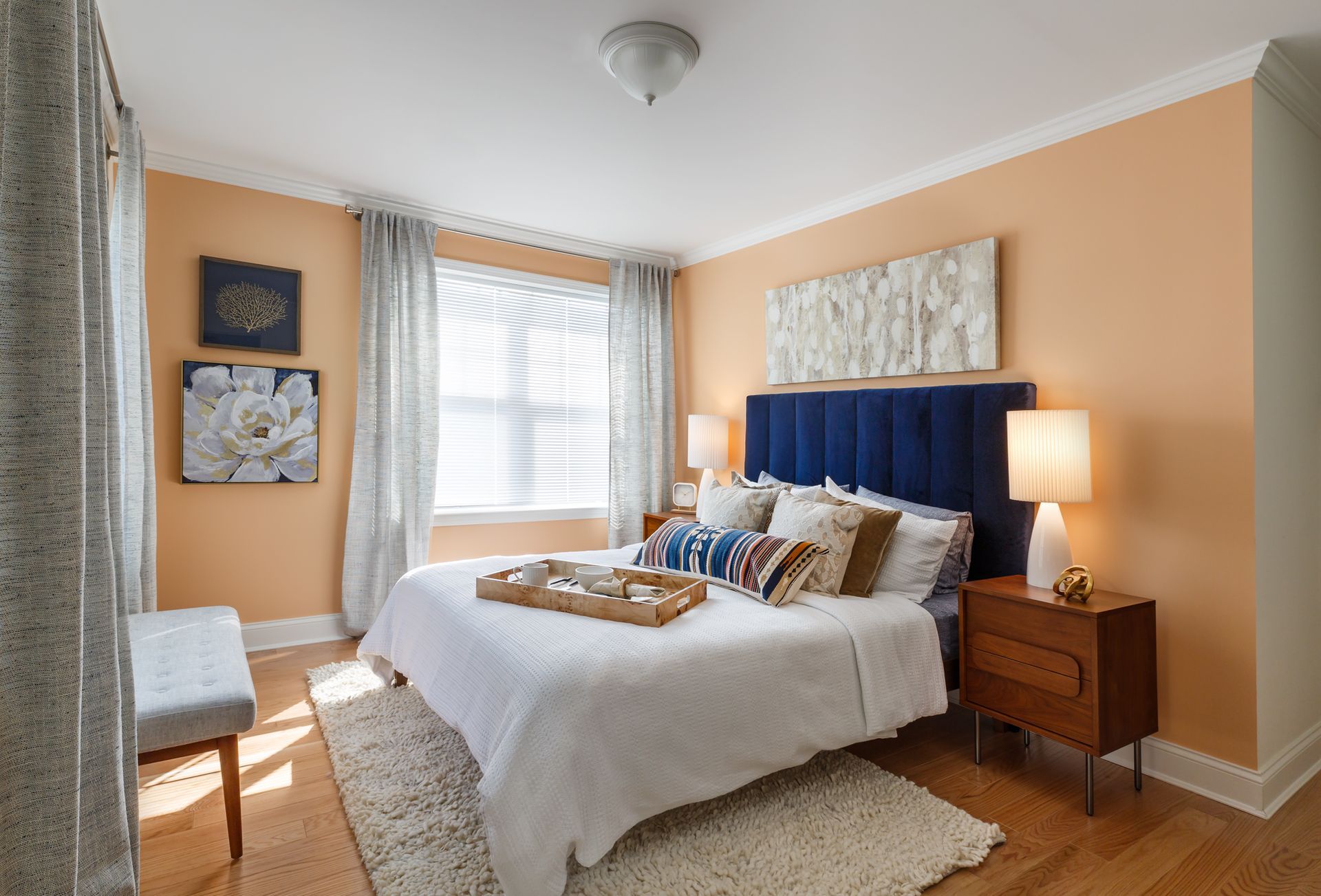 Bedroom with peach walls, white bedding, blue headboard, and wood furniture.