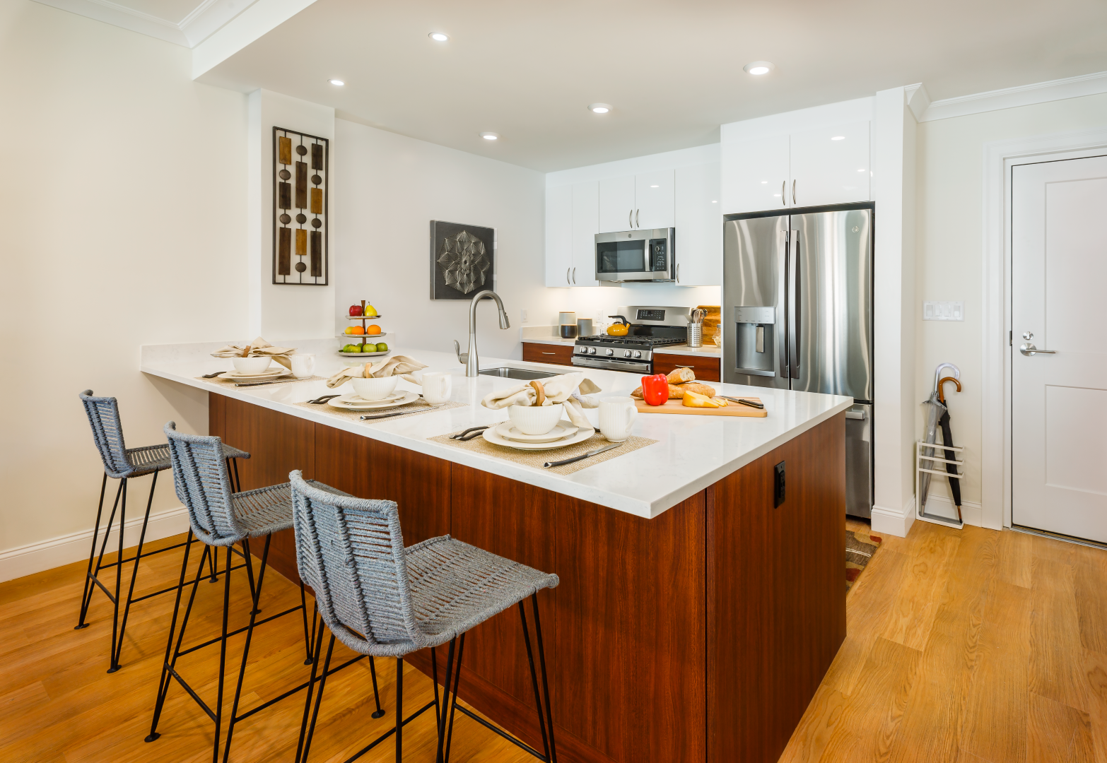 A kitchen with a large island and stools and a stainless steel refrigerator.