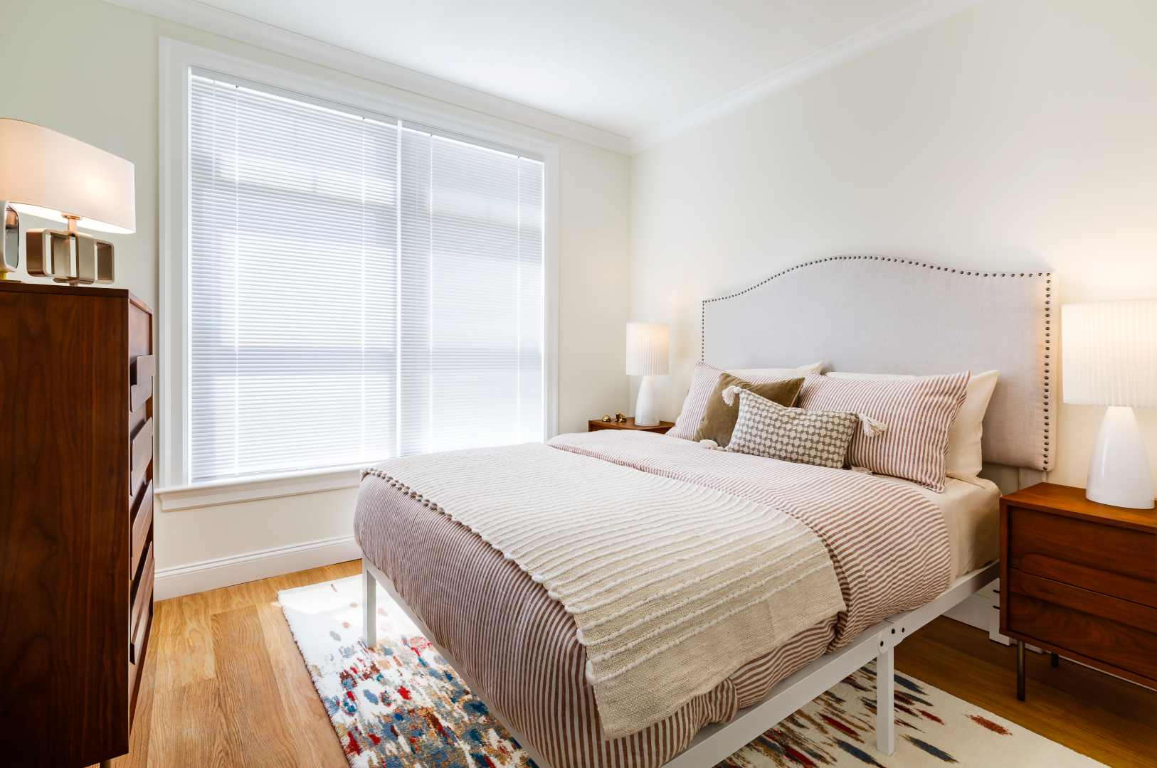 A bedroom with a bed , nightstand , dresser and window.