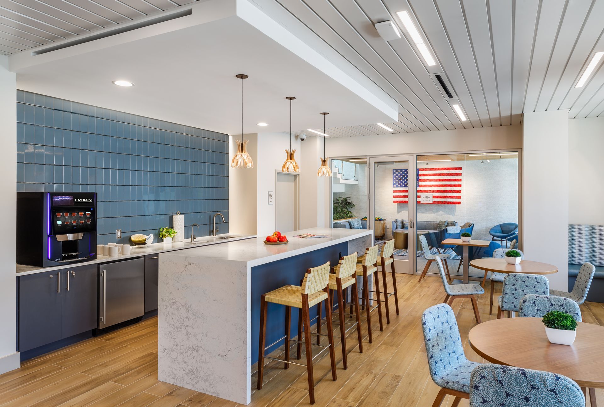 A kitchen with a large island , stools , tables and chairs.