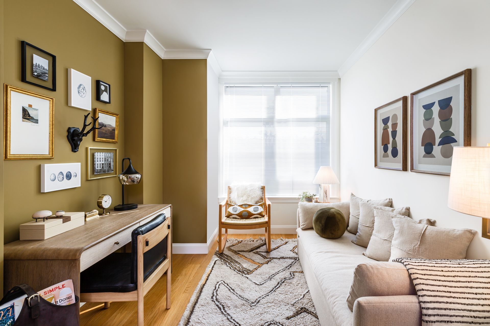 Cozy home office with desk, couch, and wall art. Olive green and white walls, wood floors.