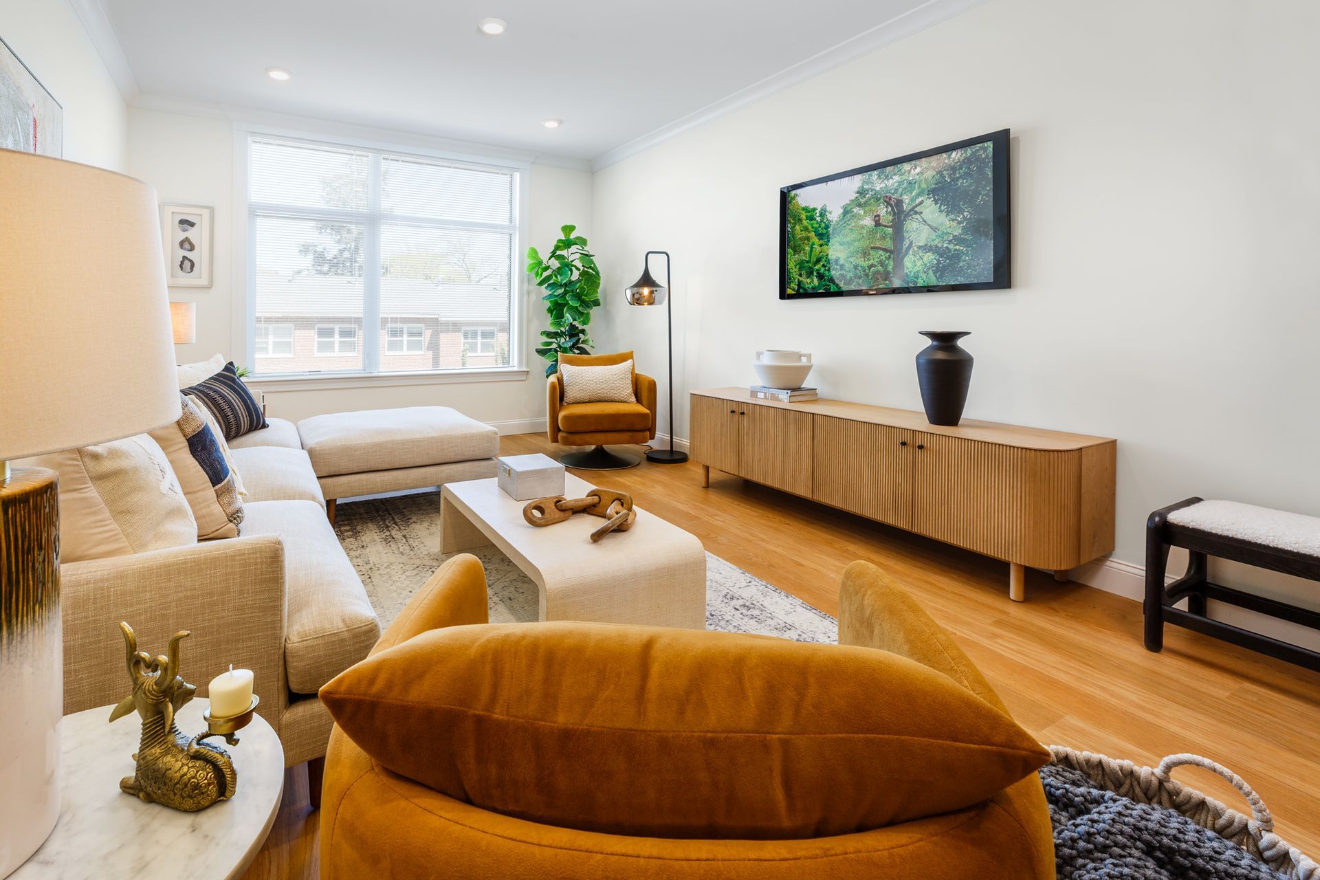 Living room with cream sofa, gold chair, wood TV console, and a large window.