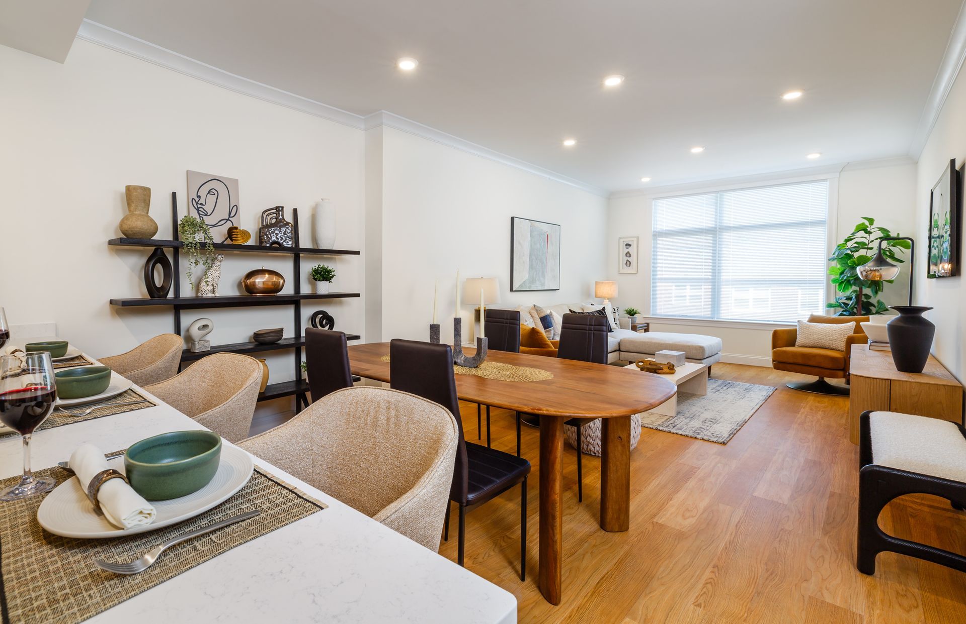 Open-plan living space with dining table and chairs, sofa, shelves with decor, and wood floors.