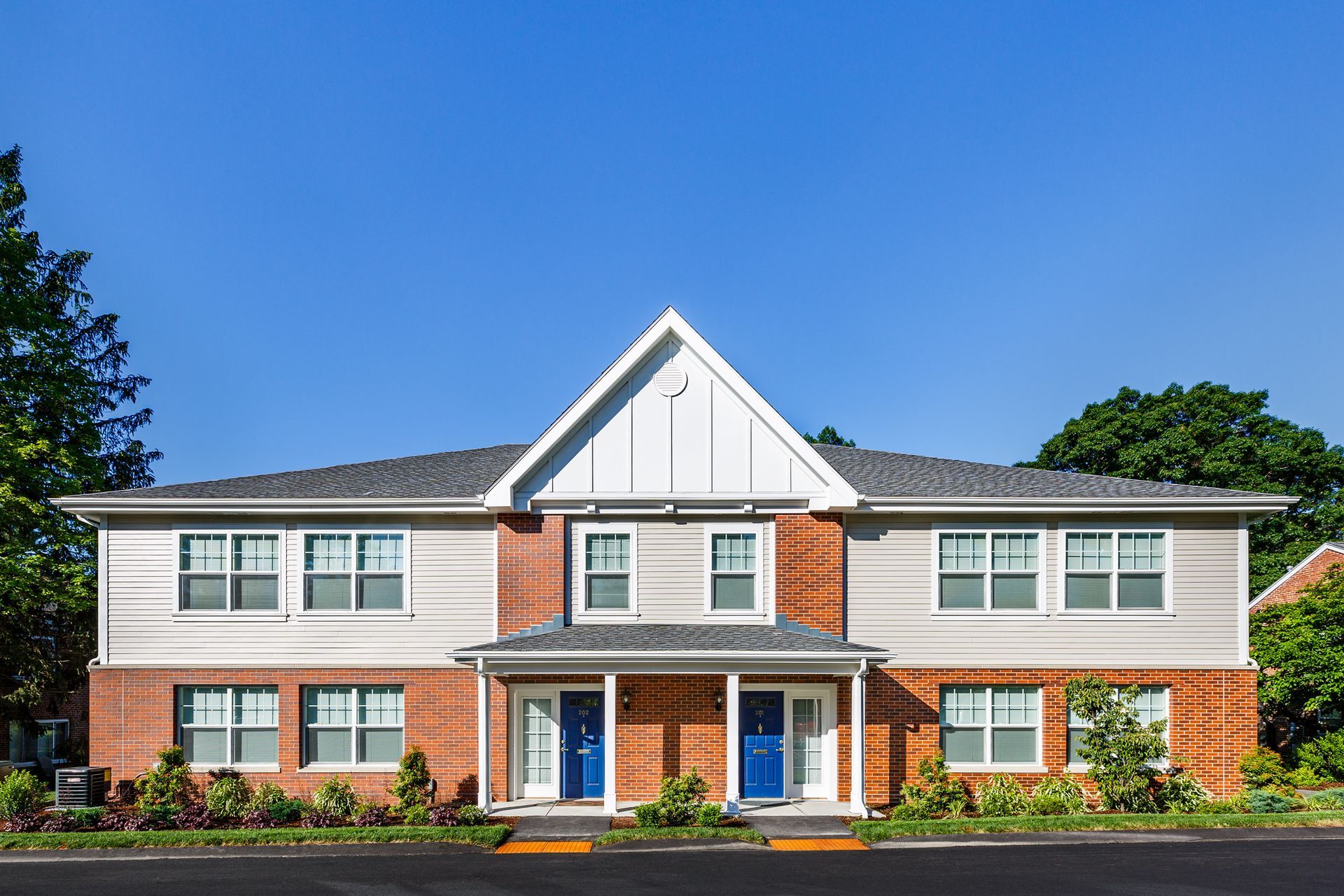 Two-story brick and metal duplex with blue doors, under a clear blue sky.