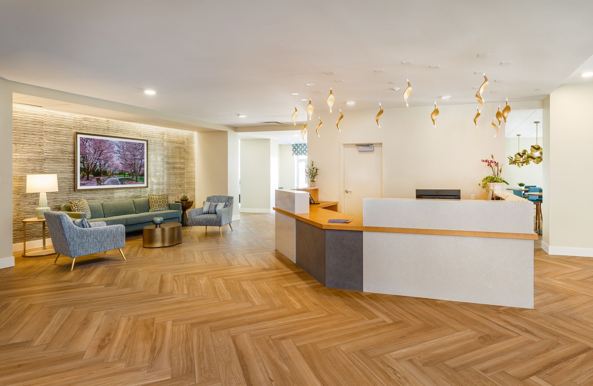 Reception area with light wood flooring, a white desk, and seating area with a sofa and armchairs.