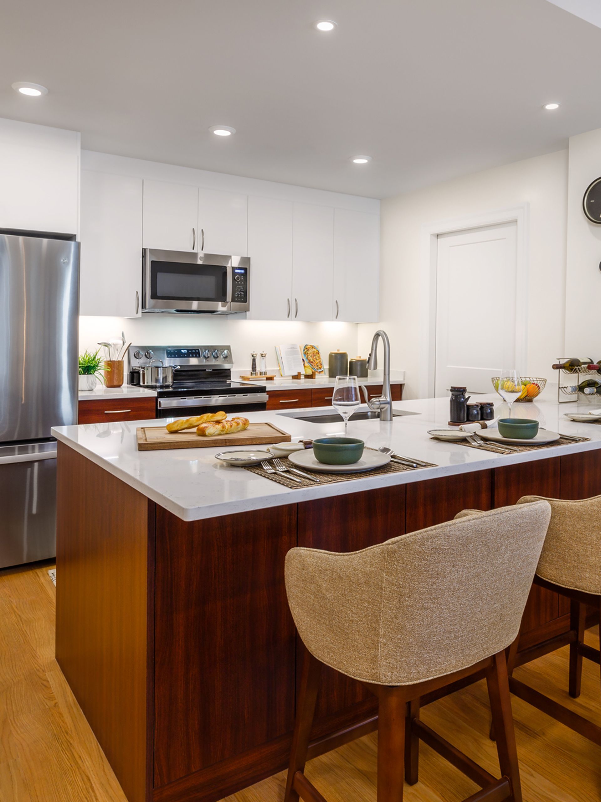 Modern kitchen featuring a wooden island with bar stools, white cabinetry, stainless appliances, and a marble countertop.